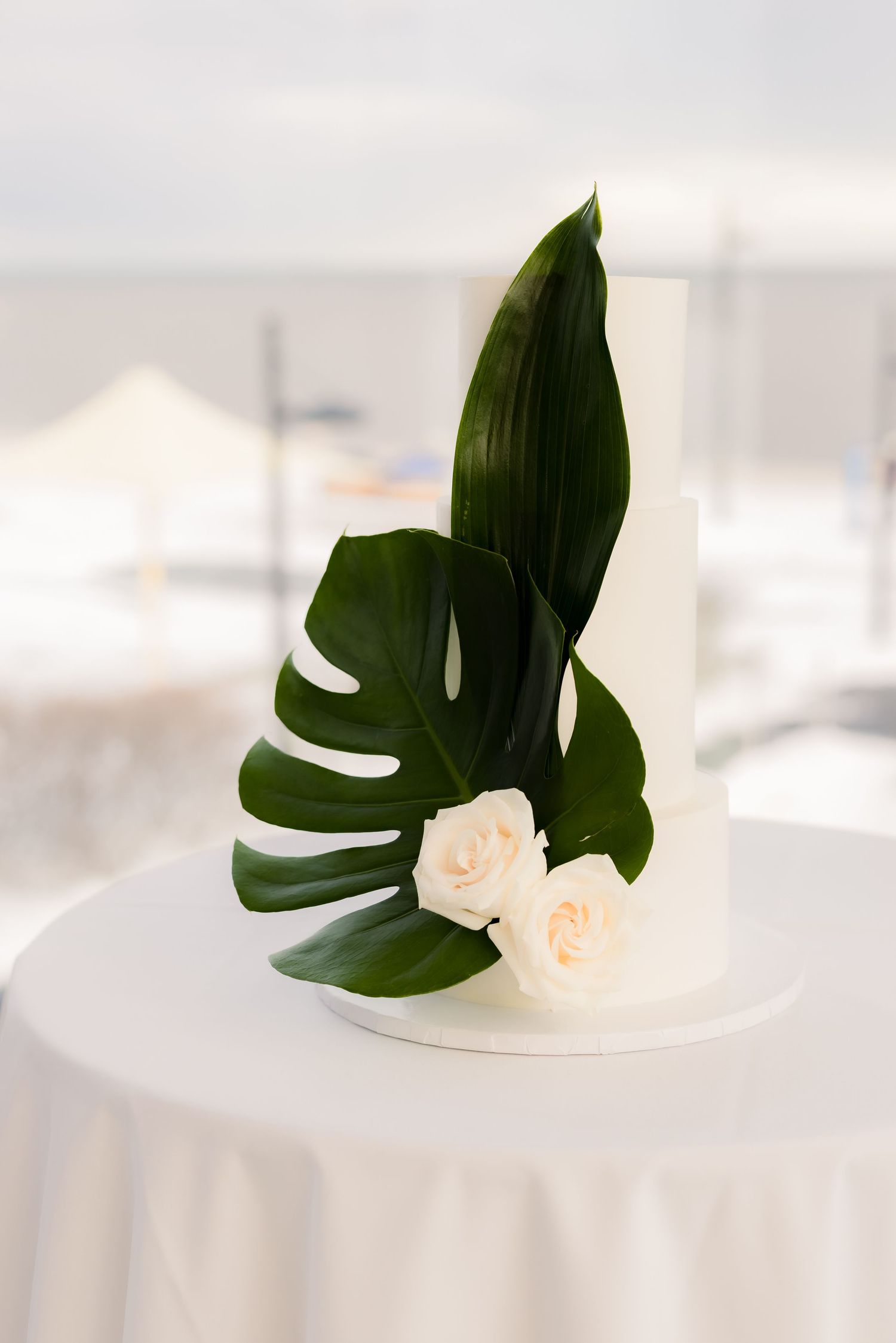Modern tropical wedding centerpiece with monstera leaf and white roses on white linen.