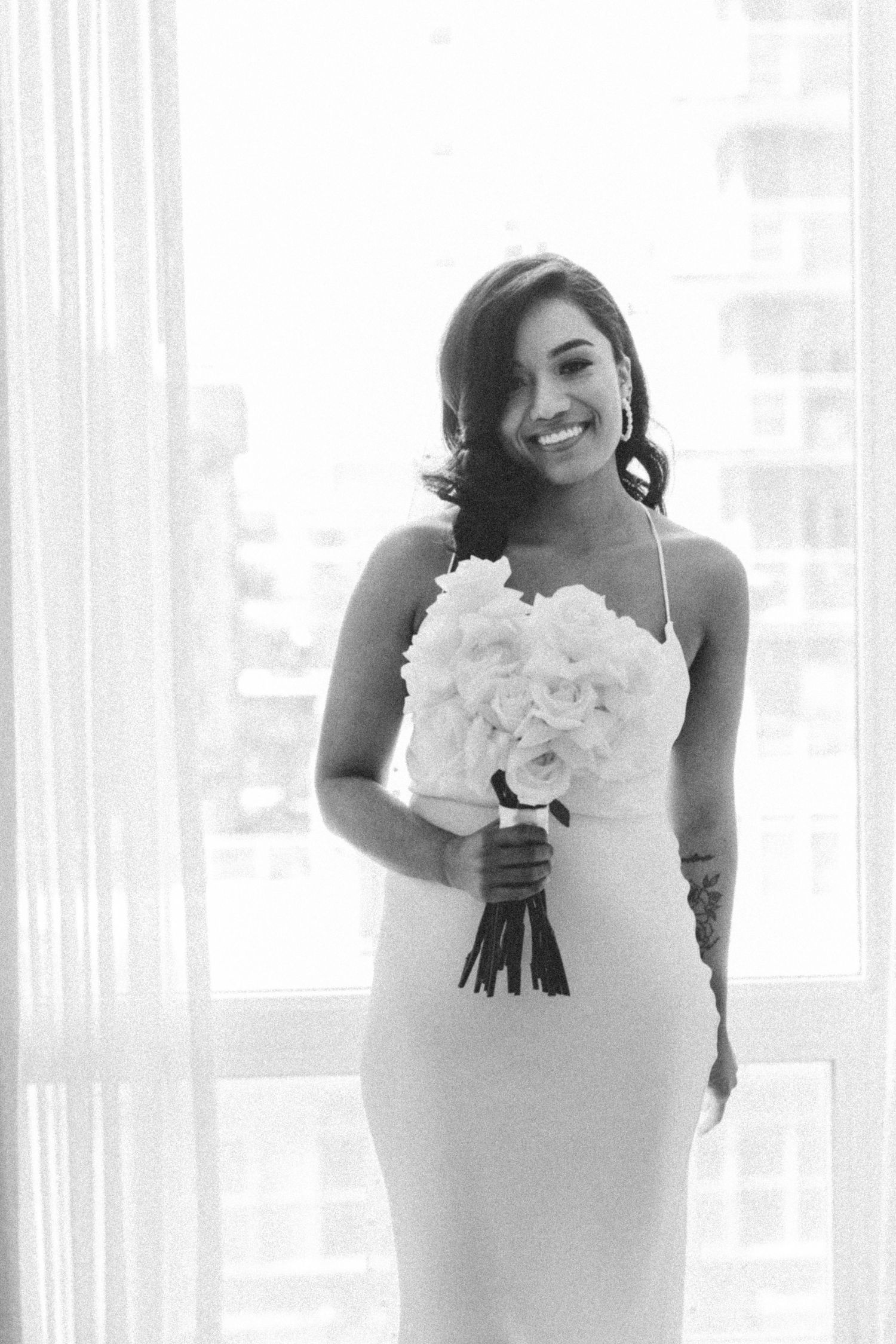 Black and white portrait of bride in fitted wedding dress holding white bouquet.