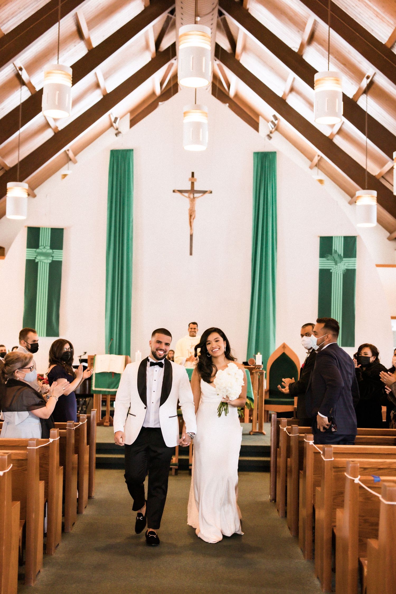 Wedding couple exits church ceremony while guests look on from wooden pews.