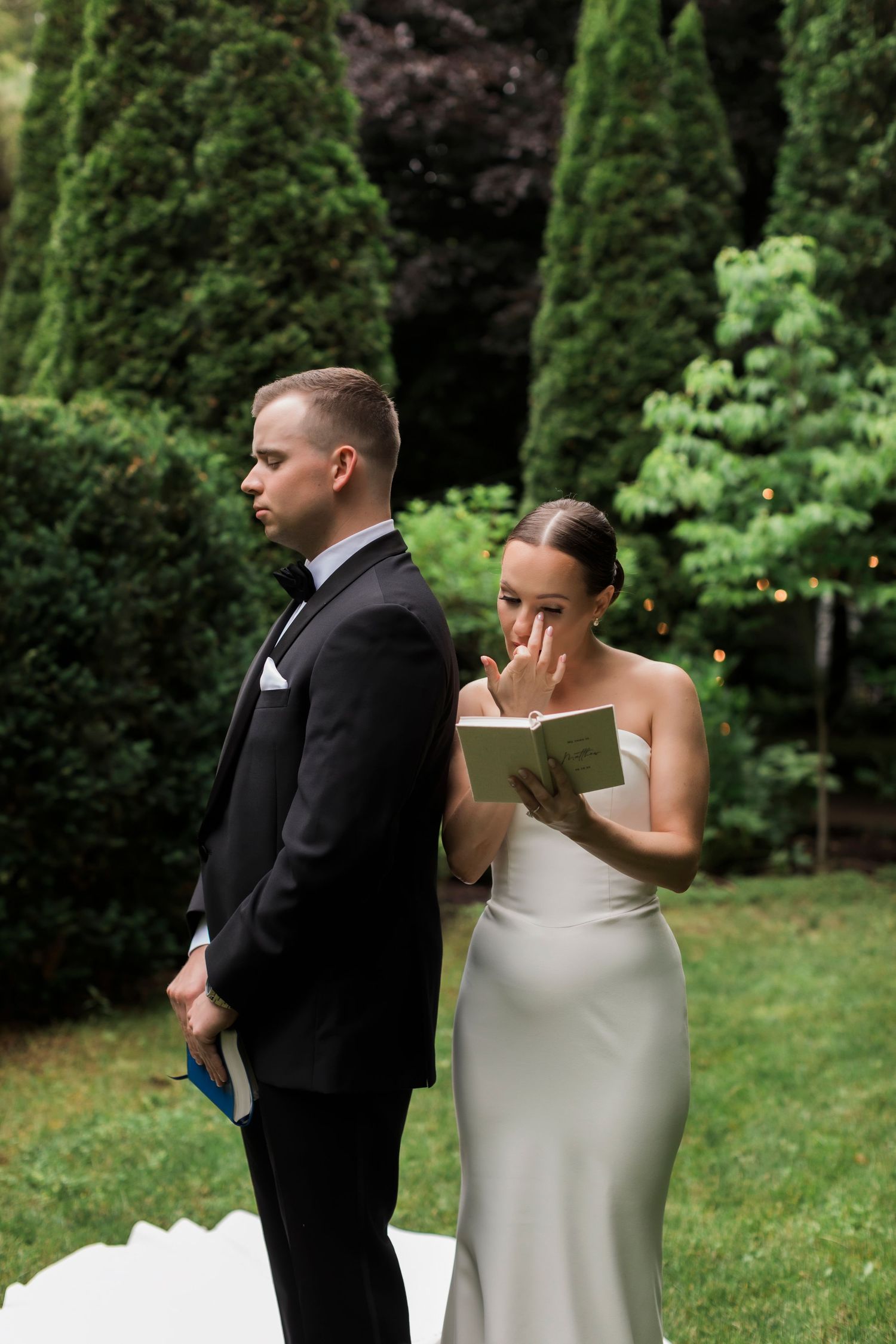 First look moment between bride and groom in a garden surrounded by evergreen trees.
