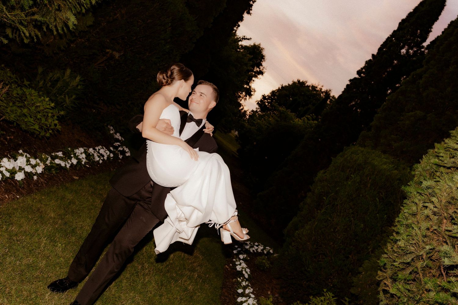 A couple shares romantic kisses and embraces in a garden setting at sunset.