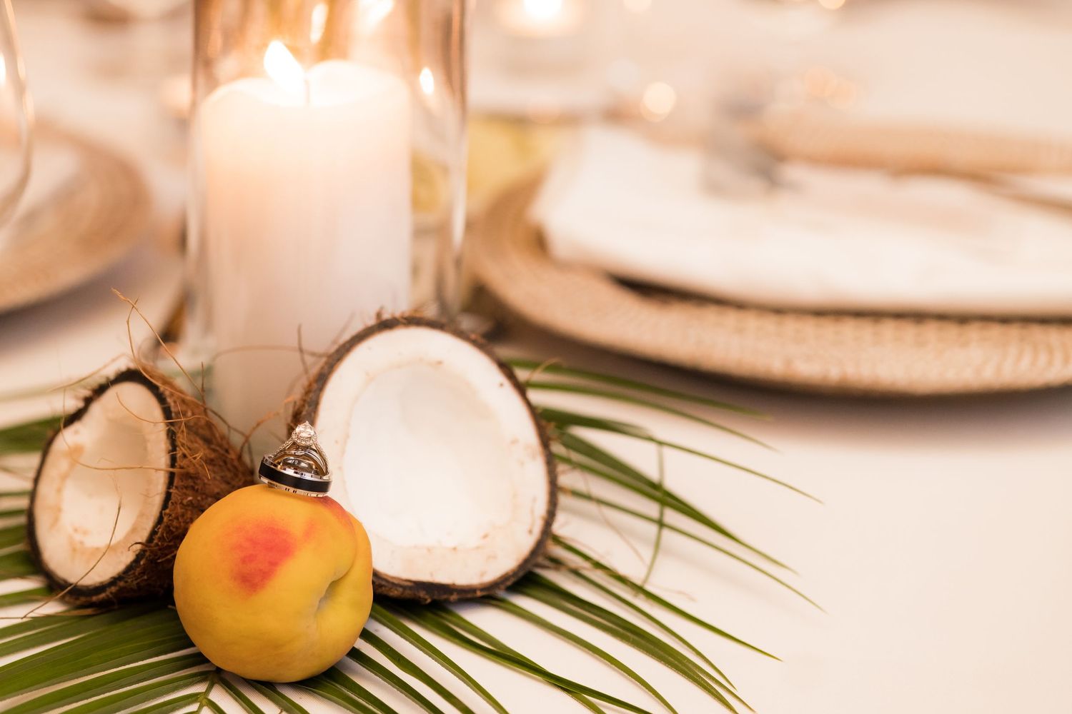 Wedding reception table decor with coconuts, fruit and palm leaves around a white candle.