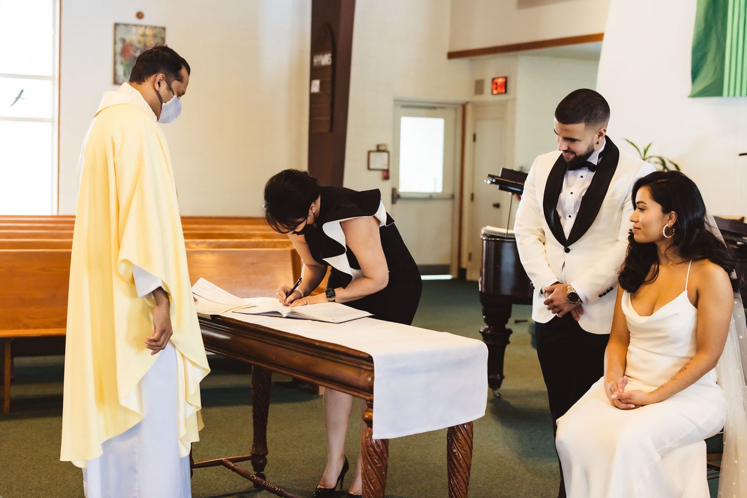 Wedding ceremony signing moment with priest and couple in church setting.