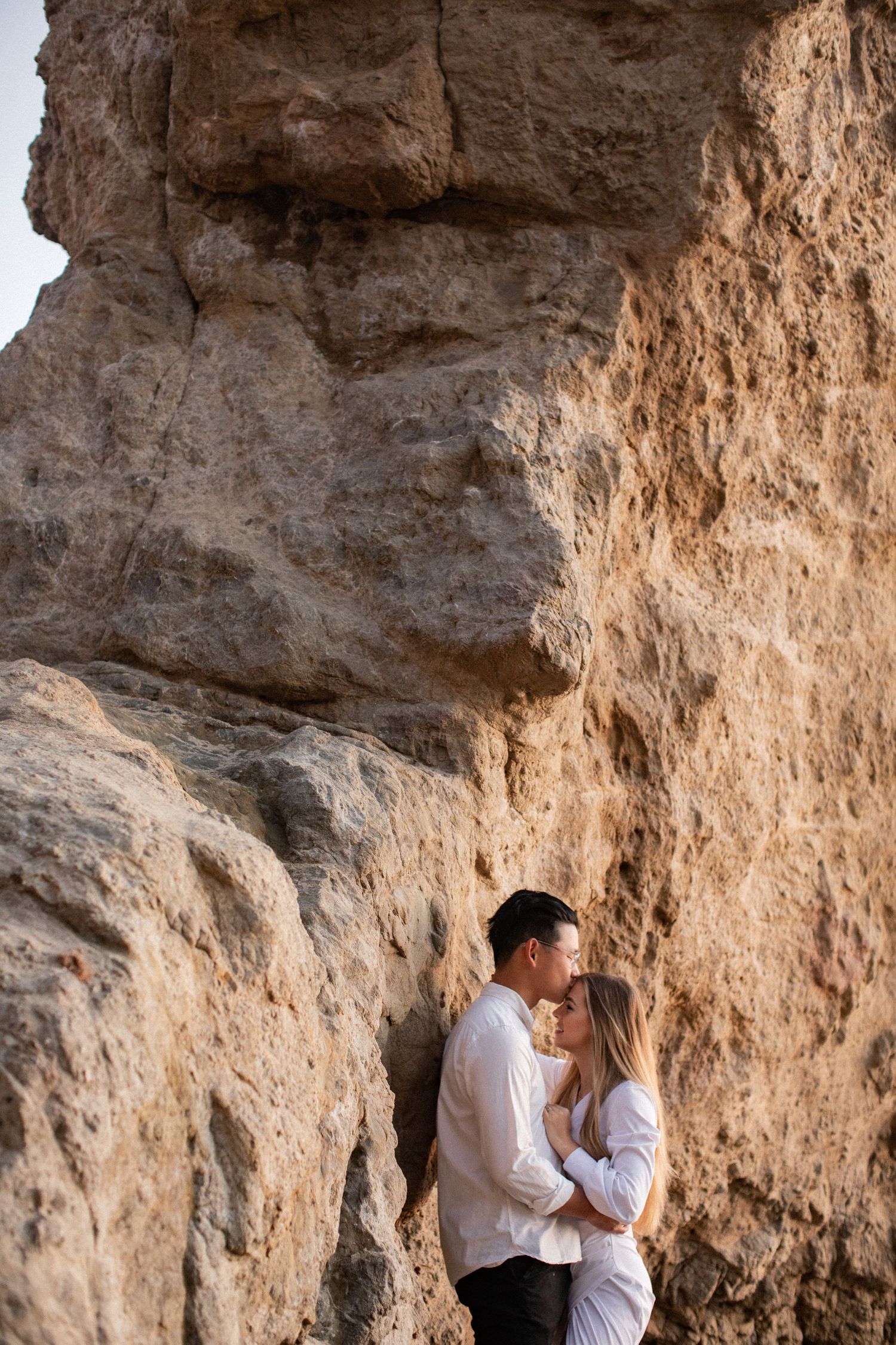 Intimate moment between couple against dramatic rocky cliff backdrop.