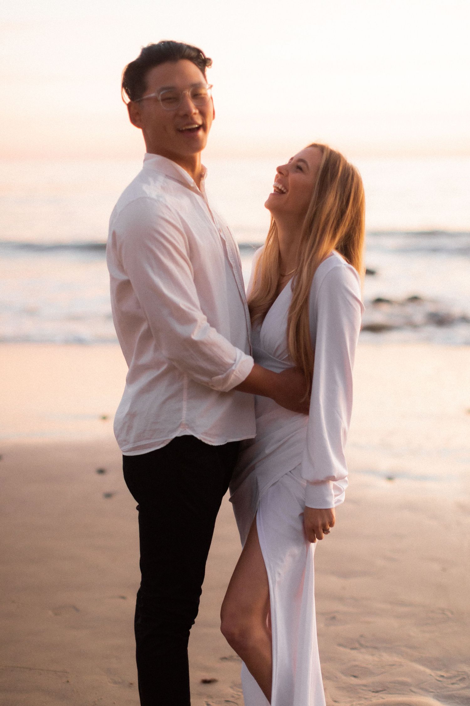 Couple in white clothing sharing intimate moment on beach at golden hour.