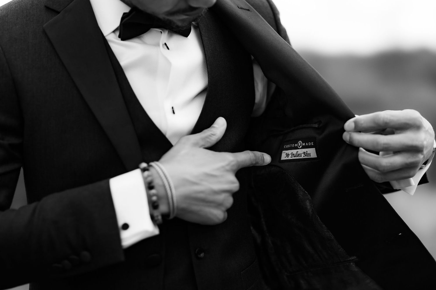Close-up black and white shot of groom adjusting his jacket pocket square while wearing a classic tuxedo.