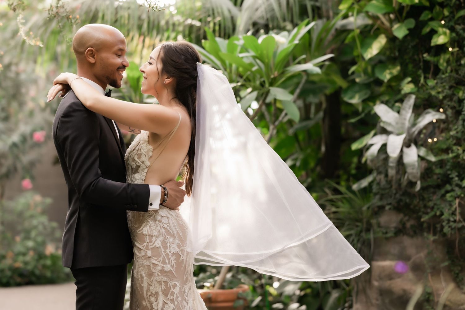 A romantic wedding moment captured in a lush garden setting with a flowing veil and elegant attire.