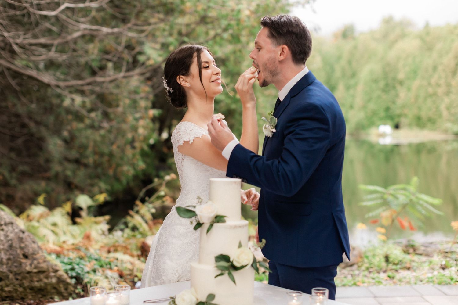 Wedding couple shares a romantic moment by a serene lake with lush greenery in the background.