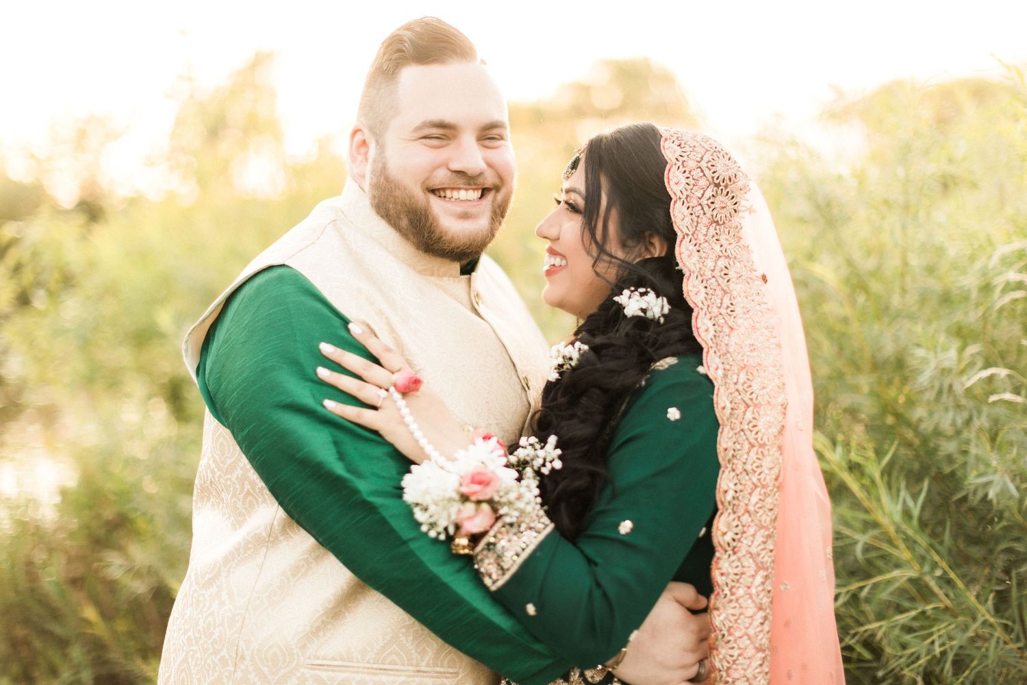 Romantic couple in winter wear embracing in golden sunlit field with flowers.