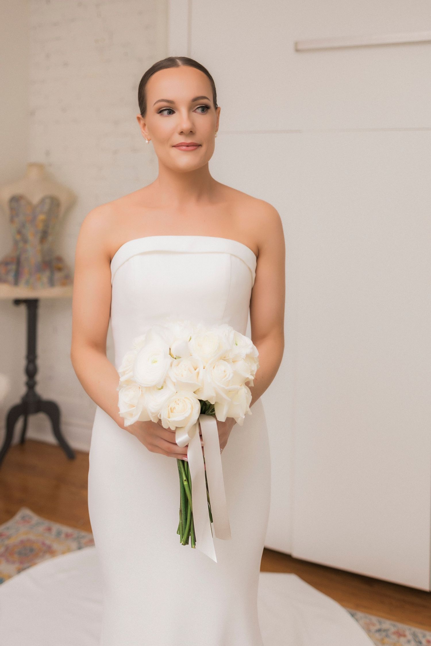 Elegant bride in white strapless gown holding a classic white rose bouquet.