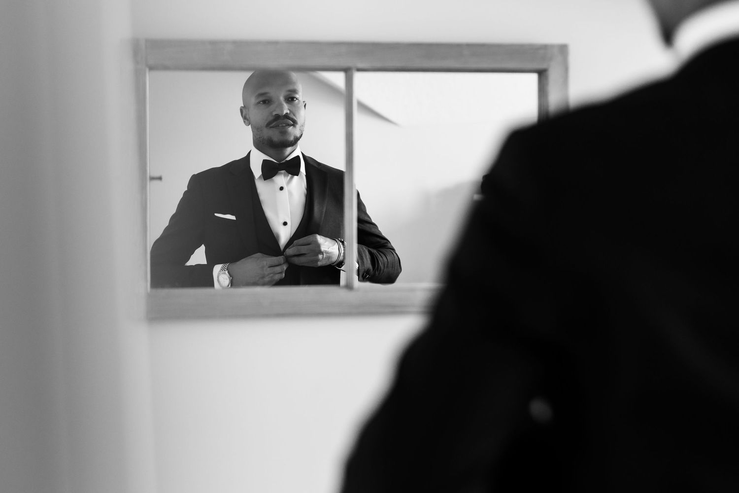 A reflection in a mirror shows a formal bowtie and suit jacket being adjusted.