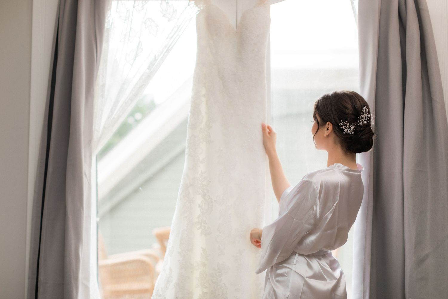 Morning of wedding preparation showing white gown hanging by window with natural light.