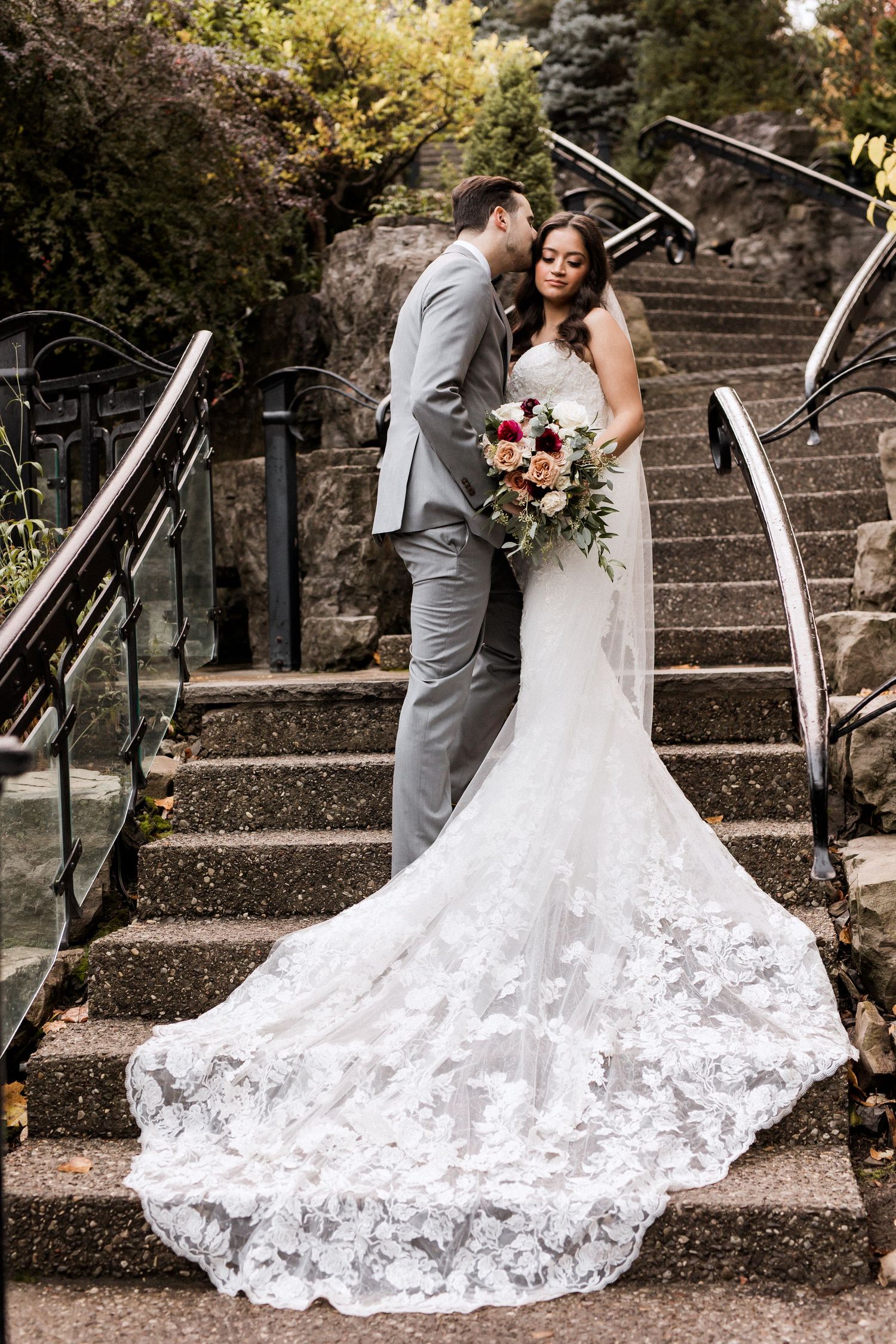 Dramatic wedding photo on stone steps showcasing intricate lace train and romantic pose.
