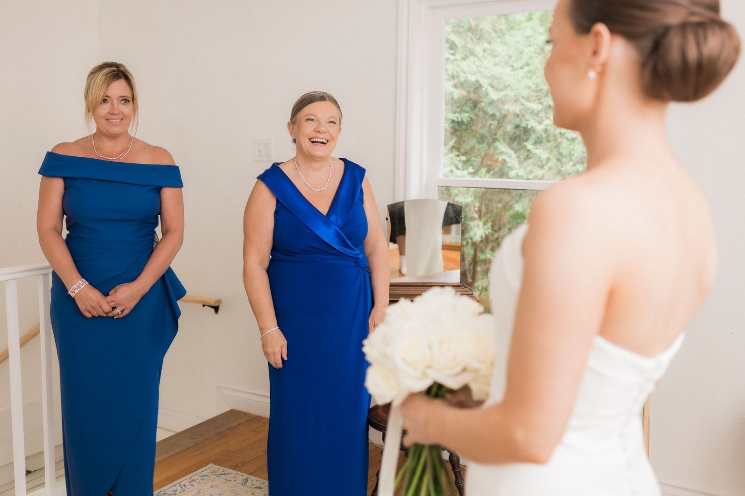 Two women in royal blue formal gowns share an emotional moment with someone in a white dress.