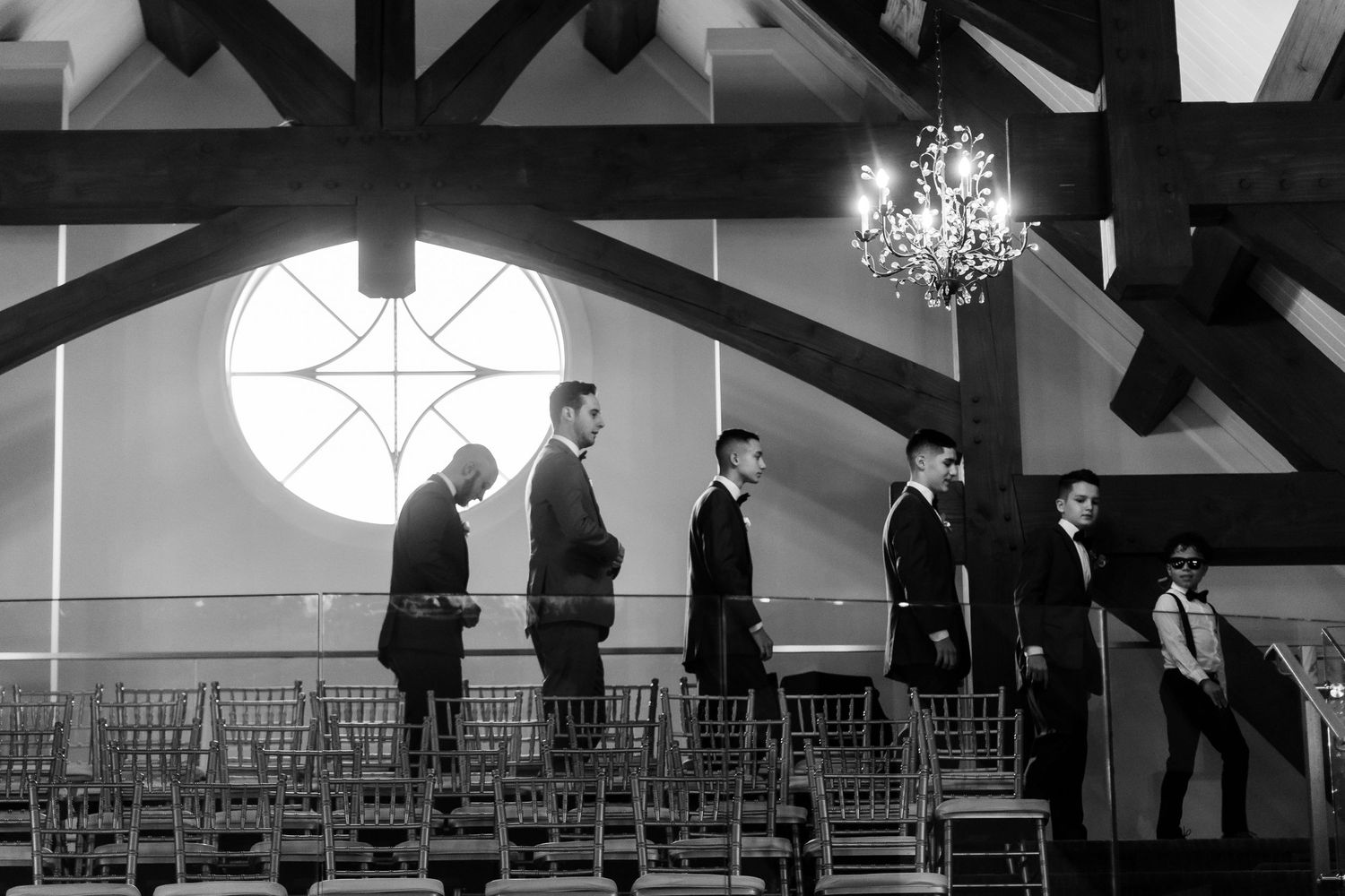 Black and white photo of wedding party members lined up in a chapel with vaulted ceilings and a heart-shaped window.