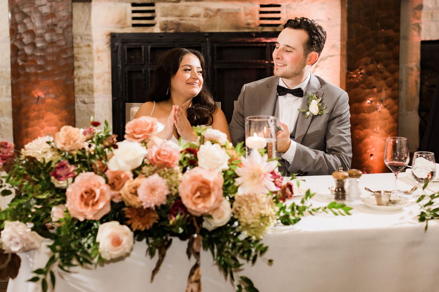 A couple sits at a wedding reception table with elegant peach and white floral arrangements.