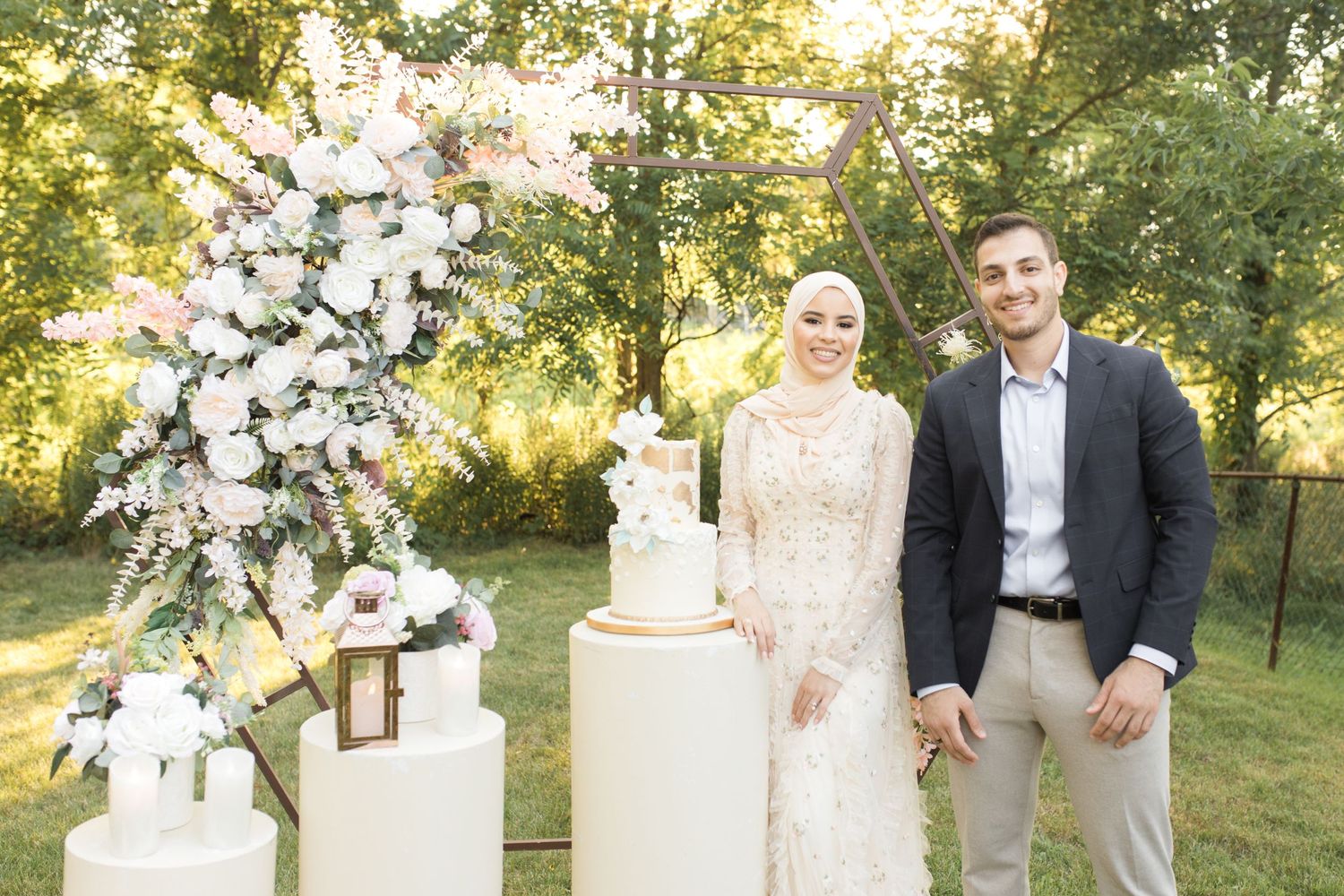 An elegant outdoor wedding display with a floral arch and tiered cake on a garden lawn.
