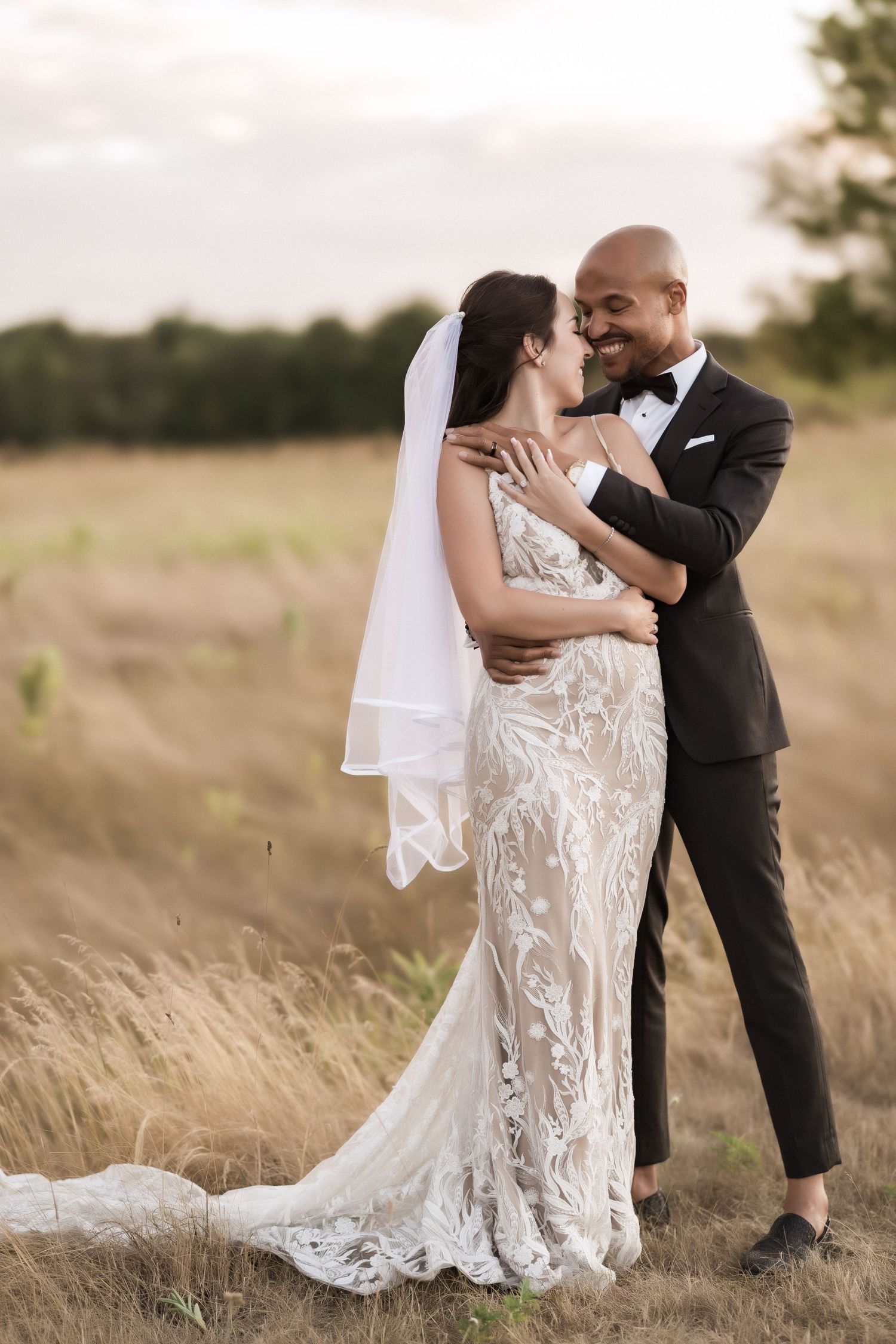Romantic wedding portrait of a couple embracing in a sun-lit field with the bride wearing a lace gown.