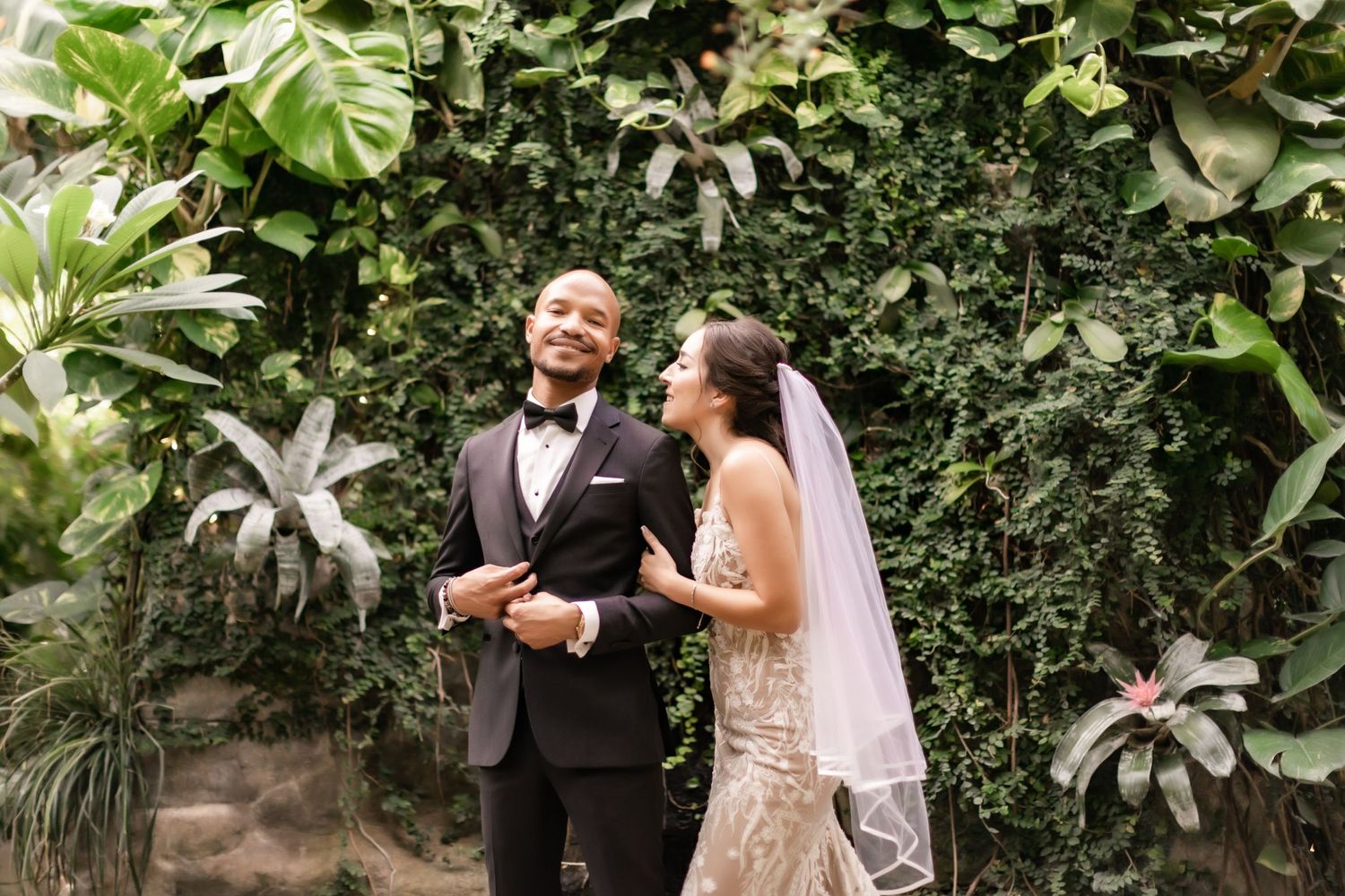 Happy wedding couple sharing a candid laughing moment against a green garden backdrop.