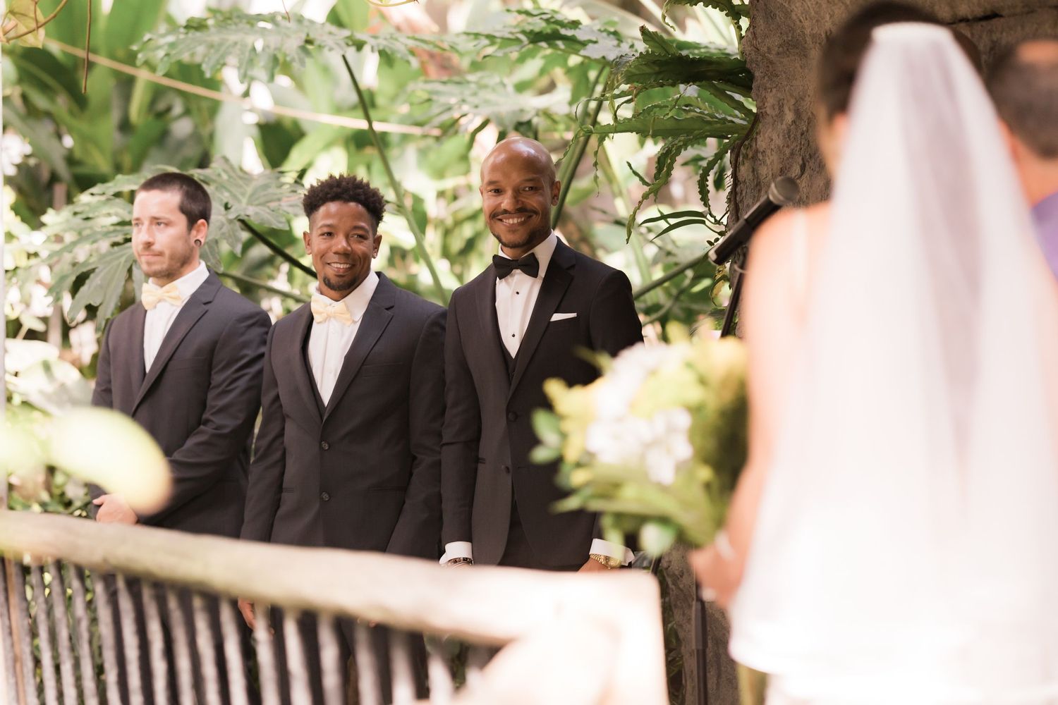 Groomsmen watching from a balcony during an outdoor garden wedding ceremony.