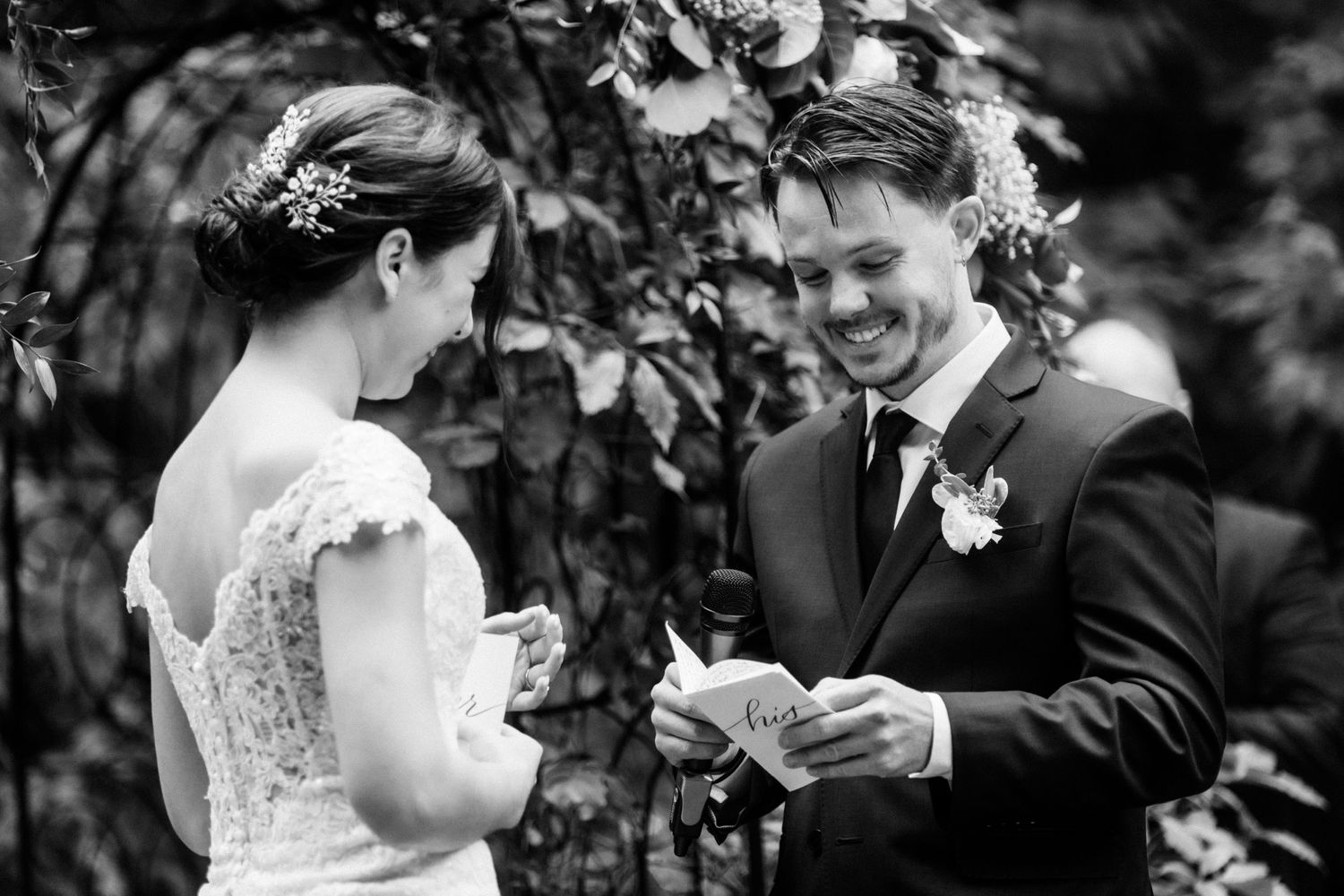 A black and white photo captures a couple exchanging handwritten vows during their garden ceremony.