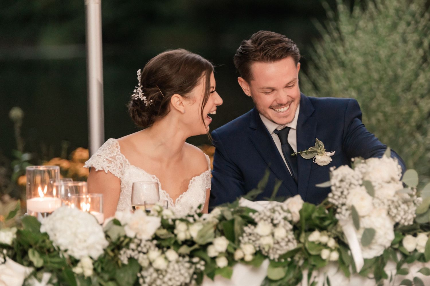 Reception table decorated with white floral arrangements as couple shares a joyful moment.