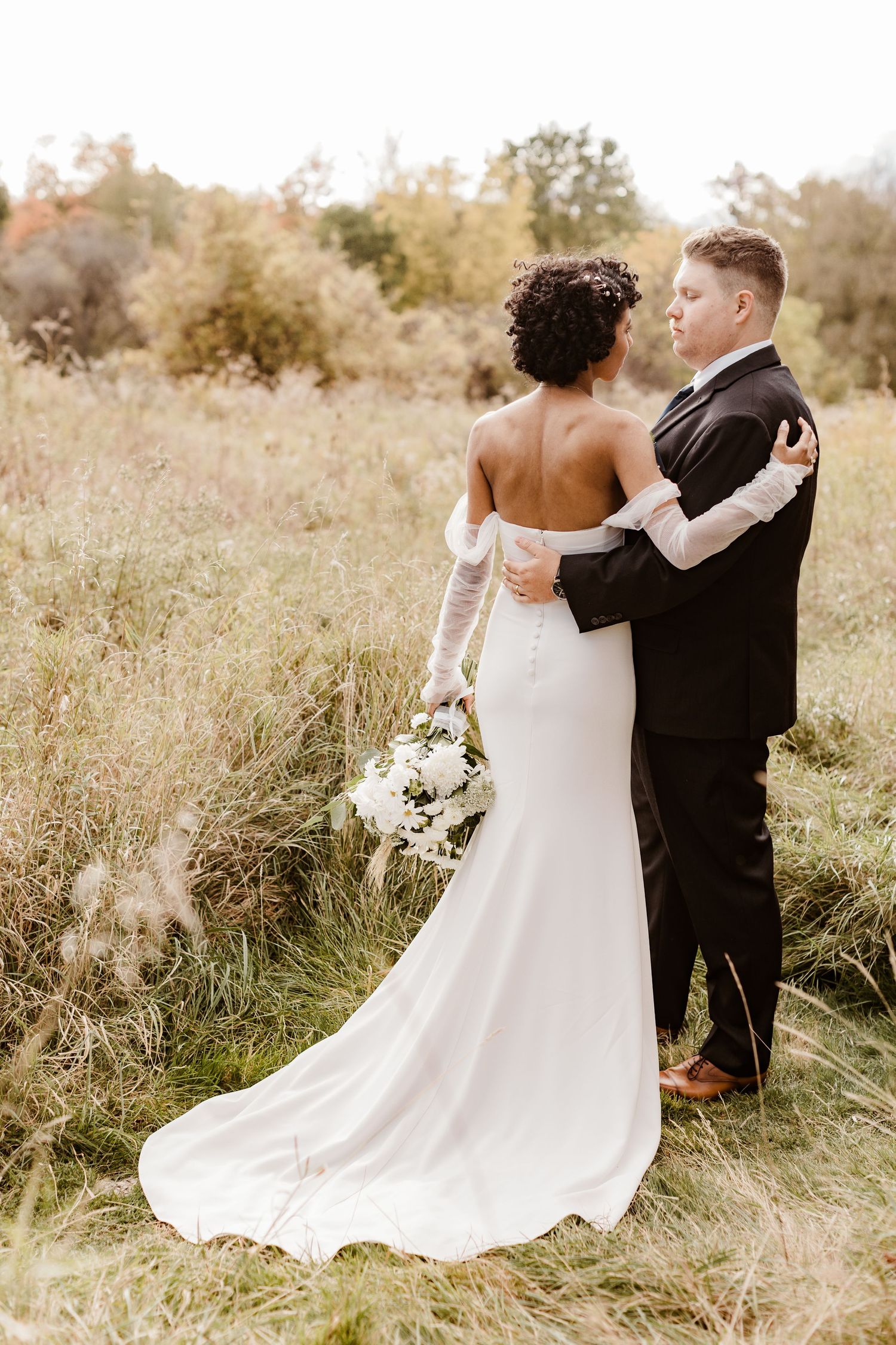 Elegant couple shares intimate moment in golden field with flowing white wedding dress.