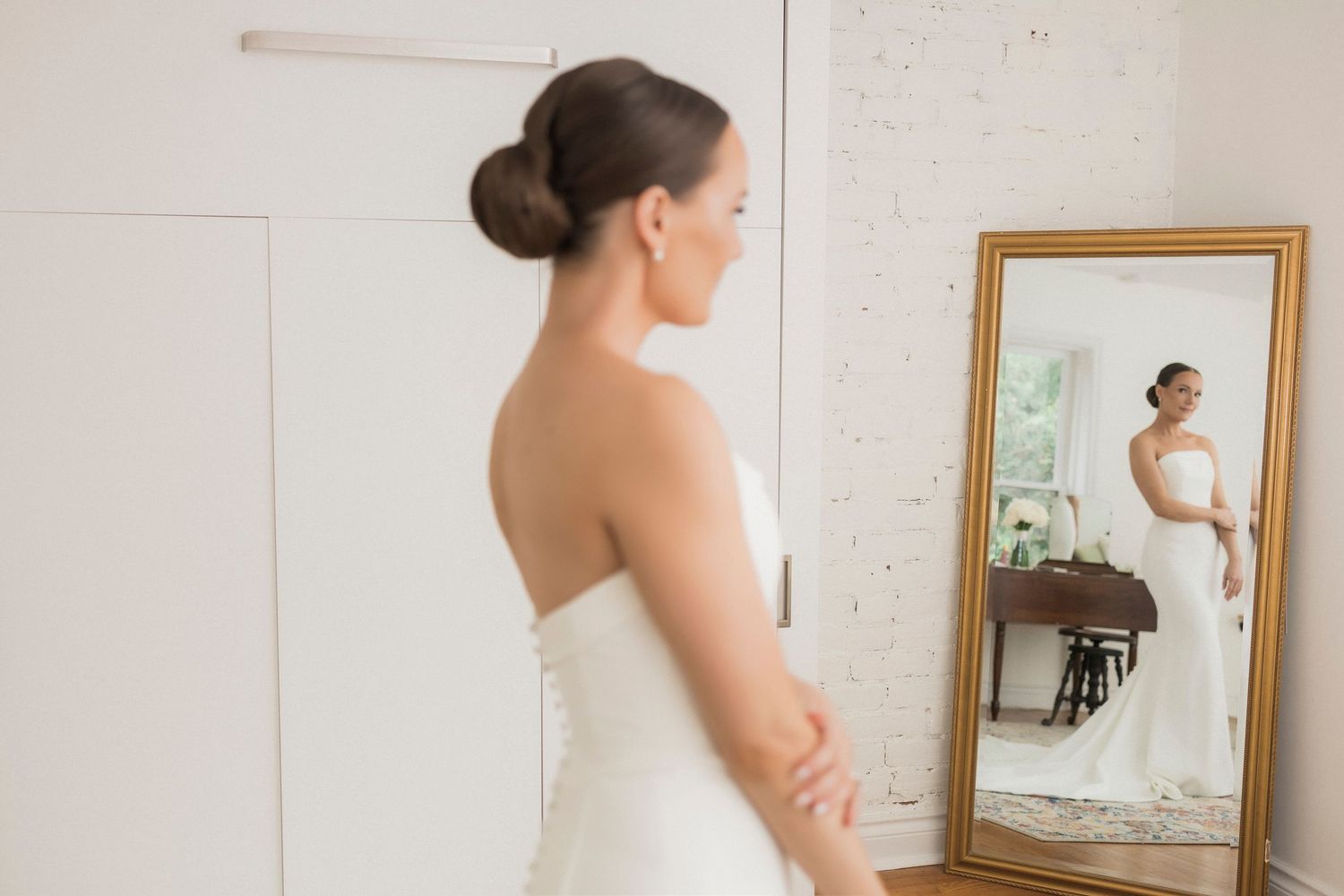 A reflection of a person in a white wedding dress standing in front of five vintage mirrors on a white wall.