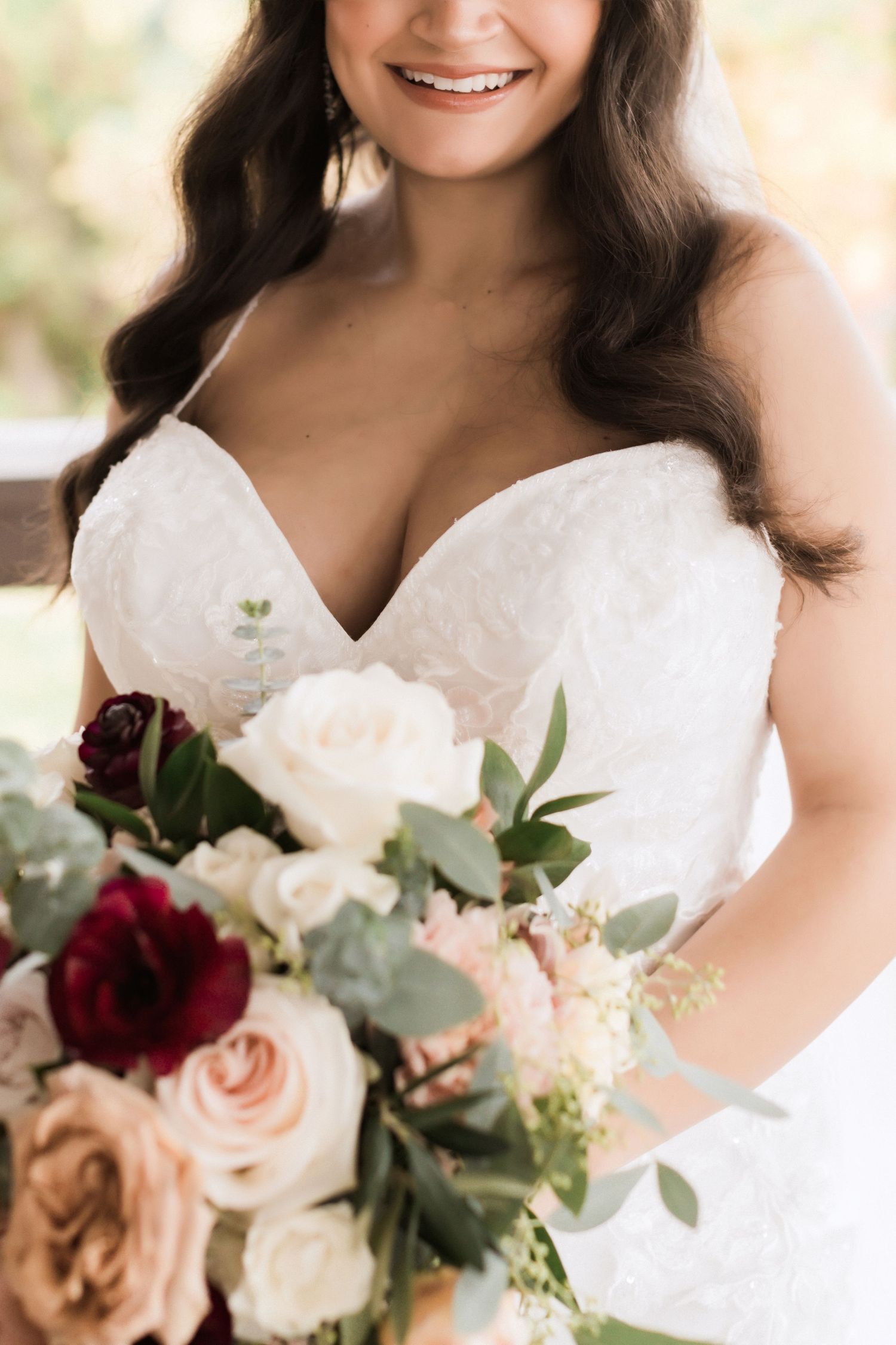 Close-up of romantic bridal bouquet with deep red and pink roses against white gown.
