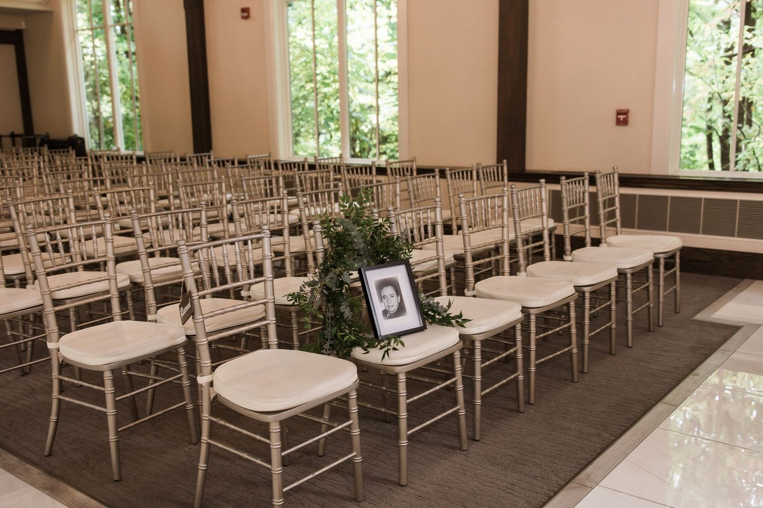 Wedding venue seating arrangement with white Chiavari chairs and memorial photo display.