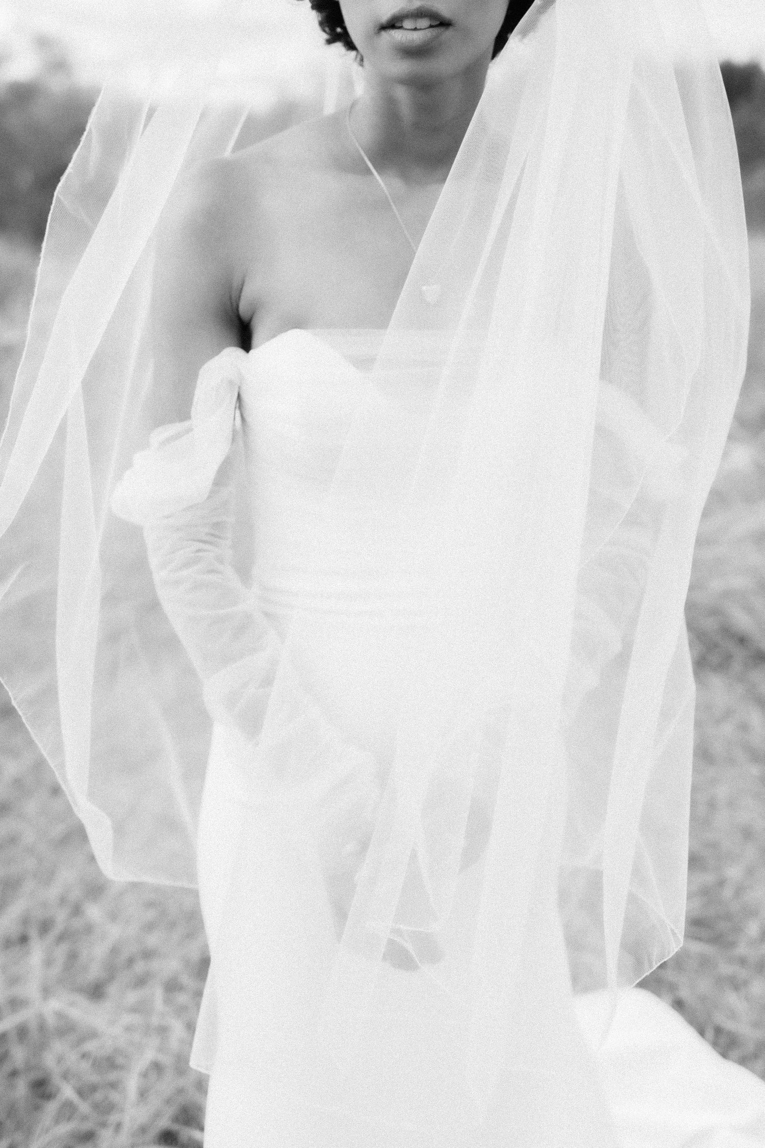 Black and white portrait of bride in strapless wedding dress with flowing veil.