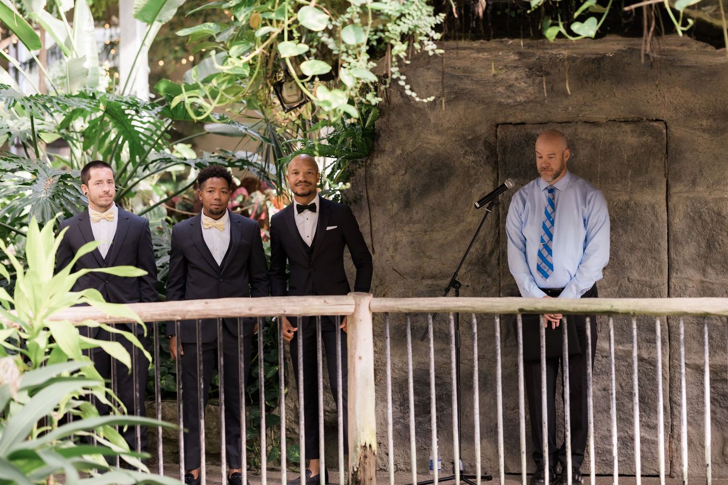 Wedding party members standing on a wooden bridge deck surrounded by greenery.