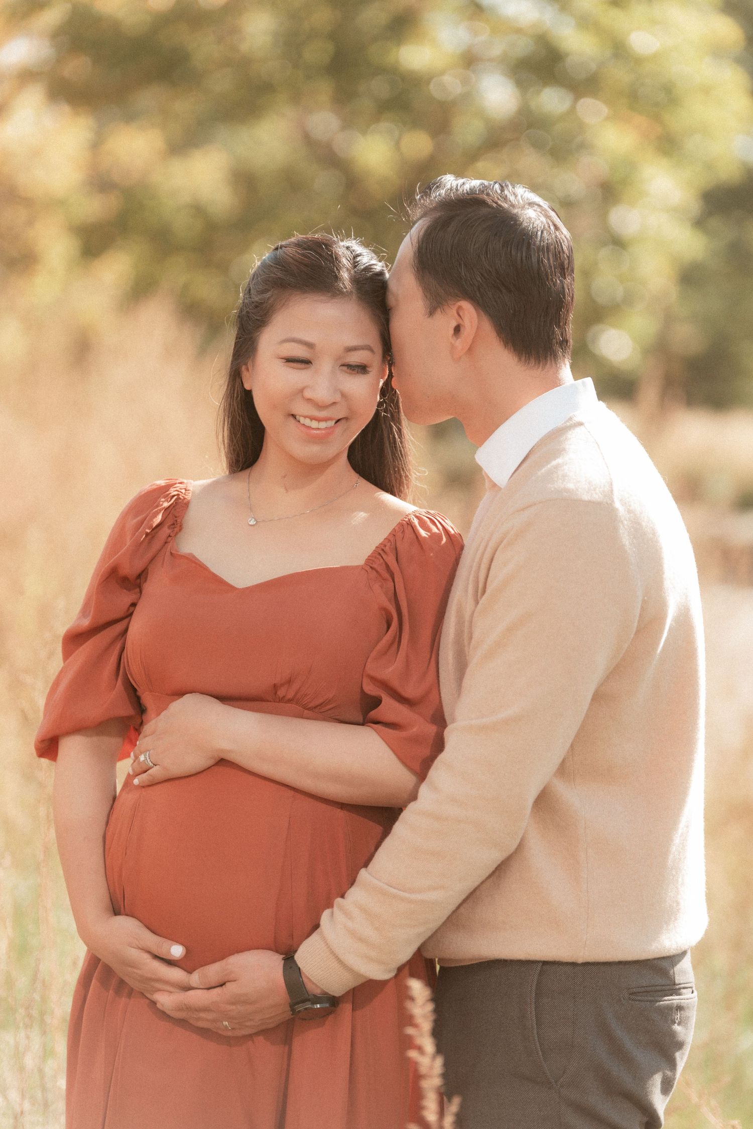Sweet maternity portrait of couple sharing loving moment in golden sunlit field.
