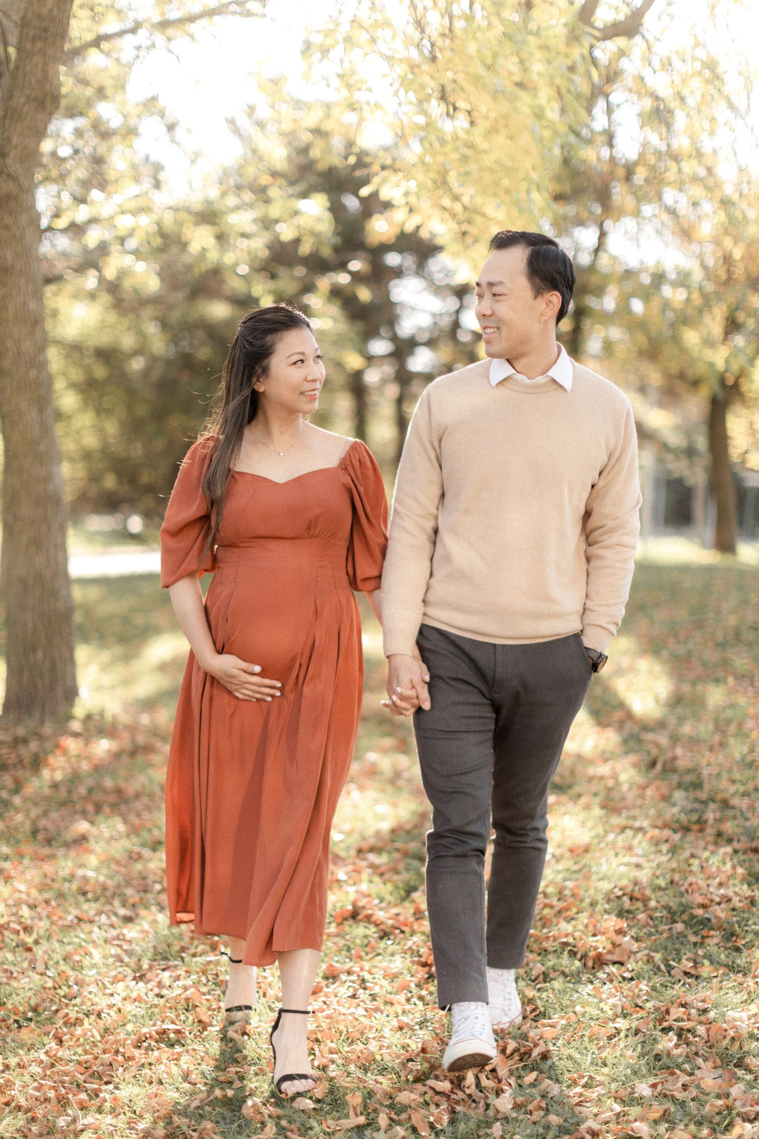 Couple takes romantic stroll through park during fall maternity photoshoot.