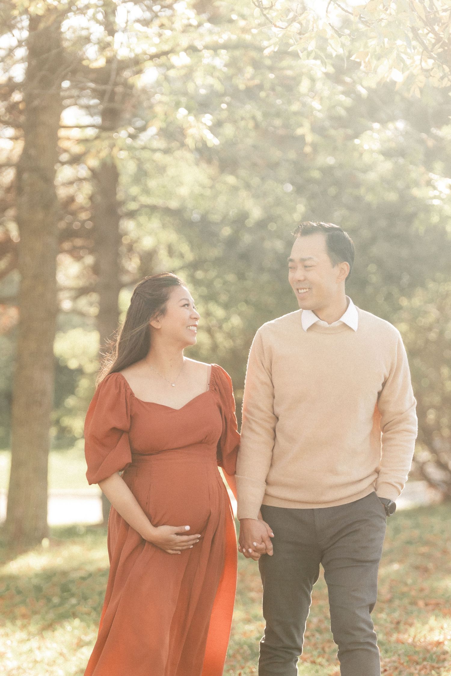 A sun-filled maternity portrait in a park with couple in matching earth-toned outfits.