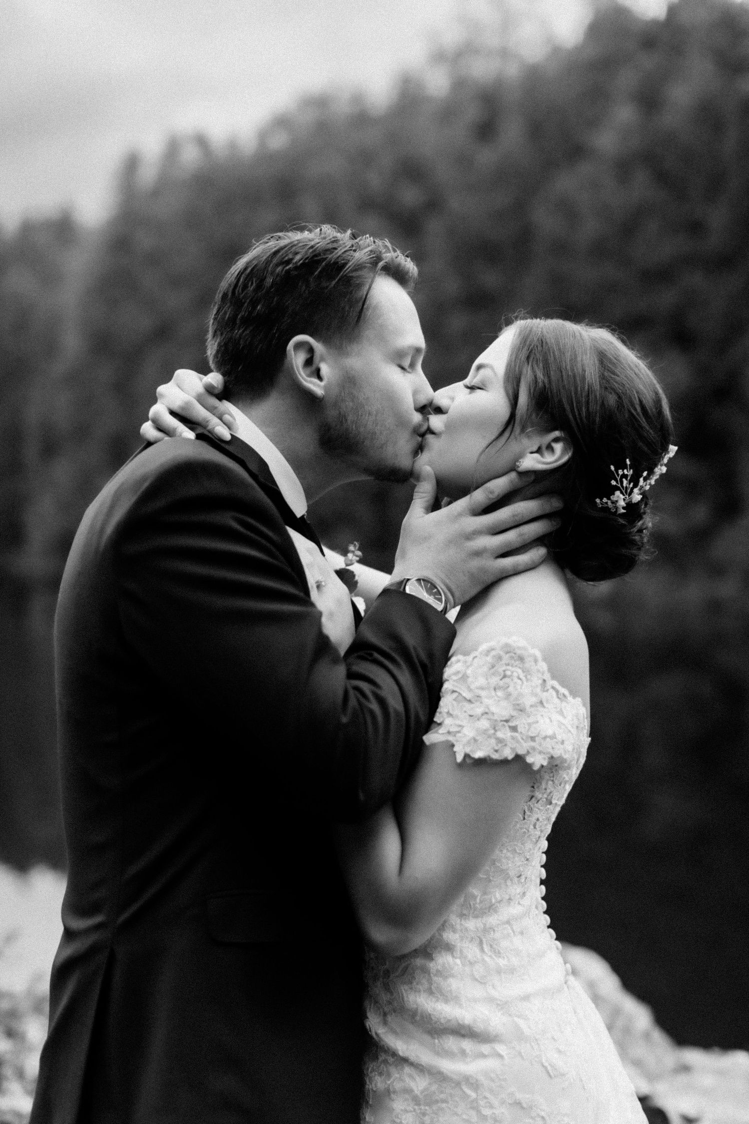 Intimate black and white wedding portrait captures tender moment against forest backdrop.