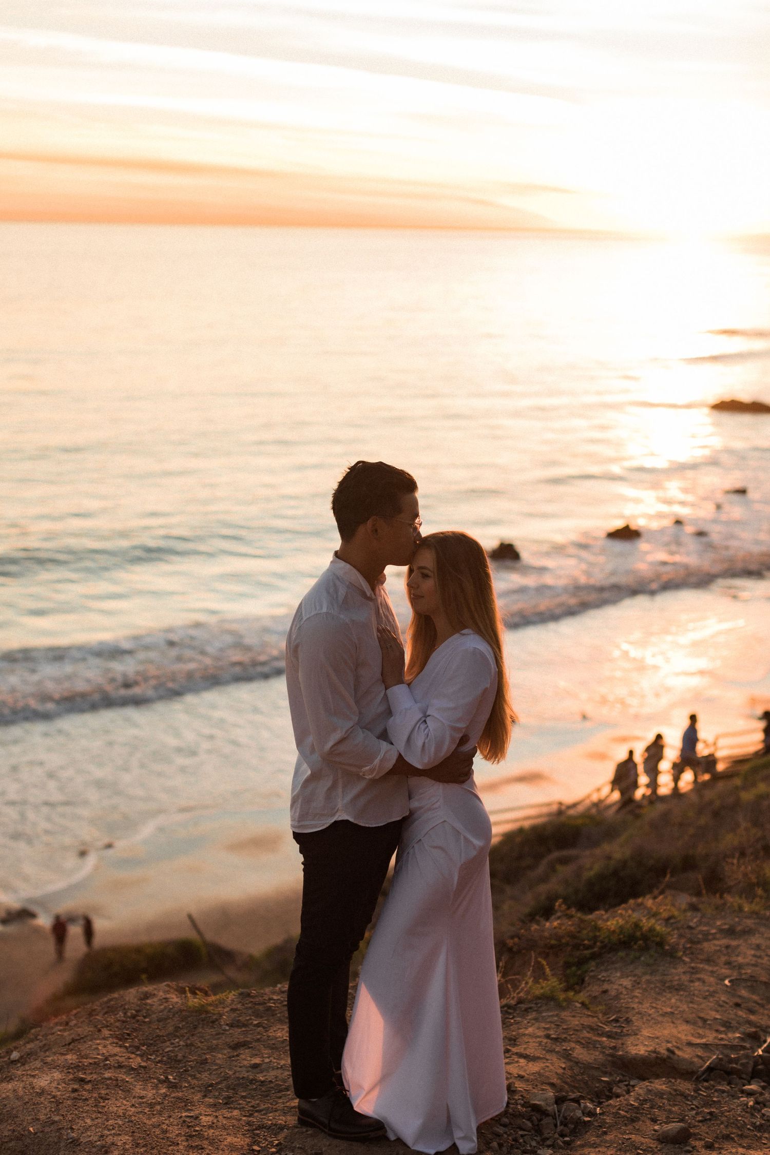 Couple shares romantic moment on cliff overlooking beach at golden hour.