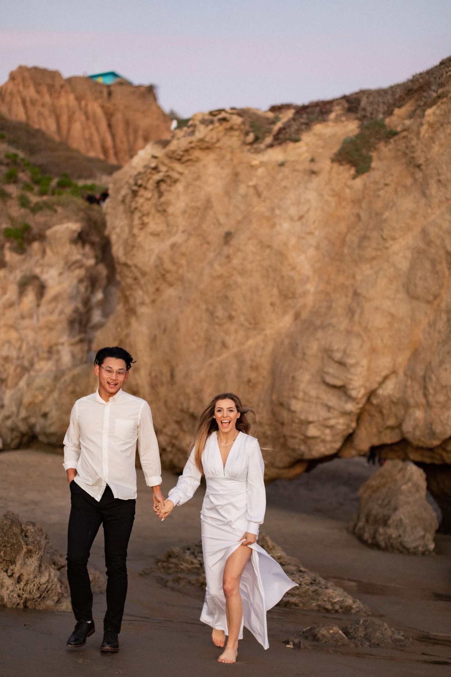 Happy couple walking and laughing together along scenic beach path.