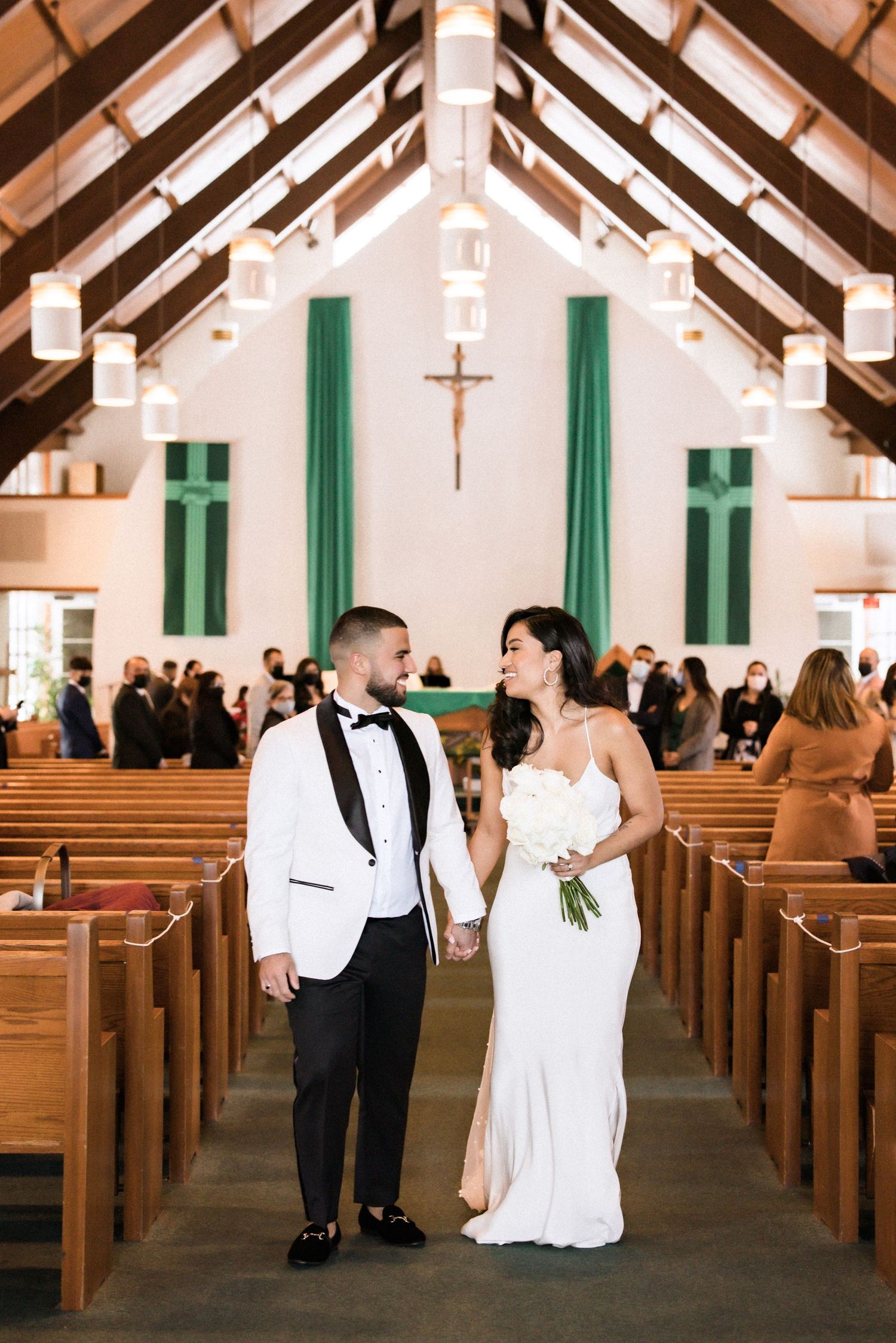 Bride and groom walk down church aisle decorated with green banners and wooden pews.