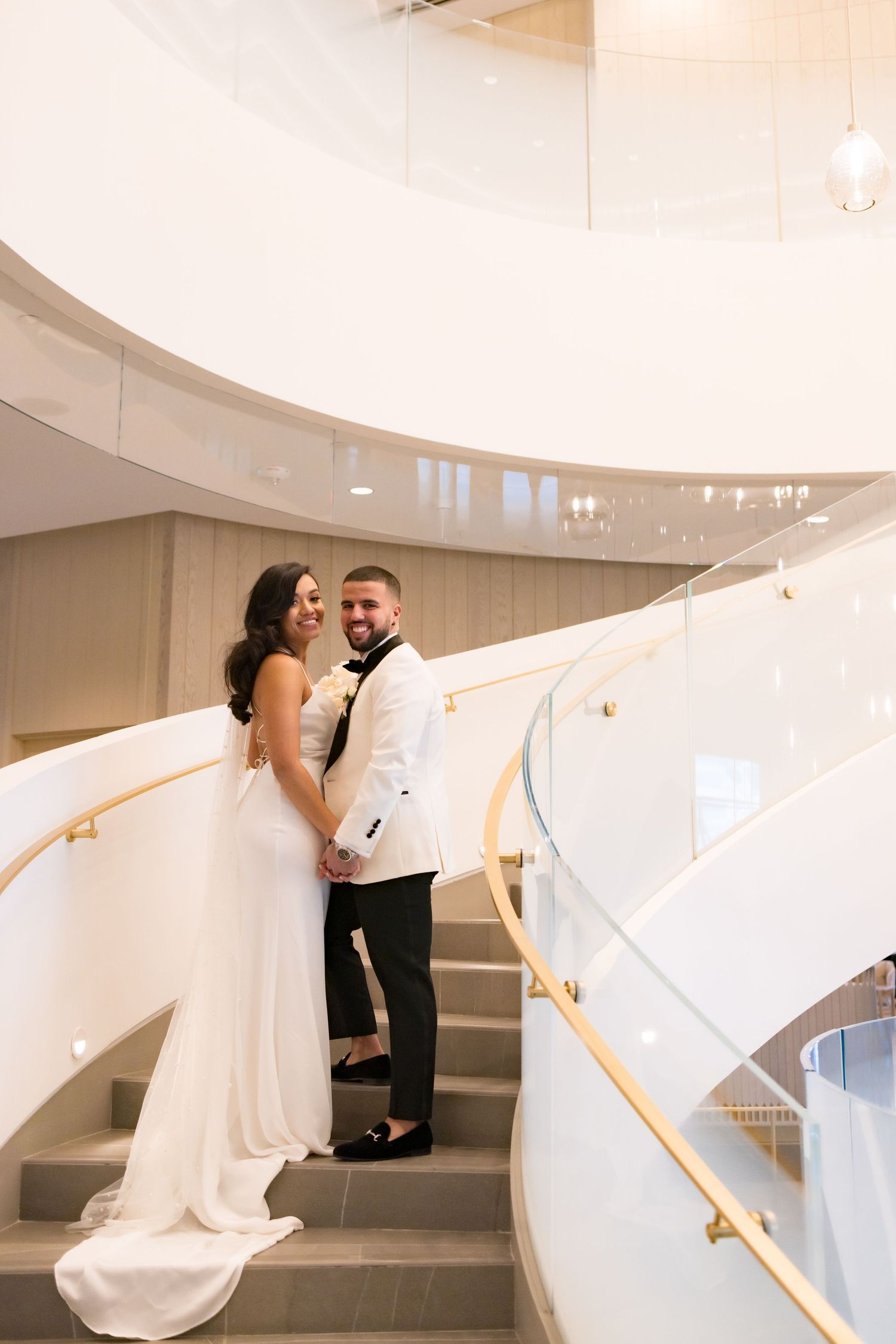 Elegant wedding portrait on curved white staircase with modern pendant lighting.