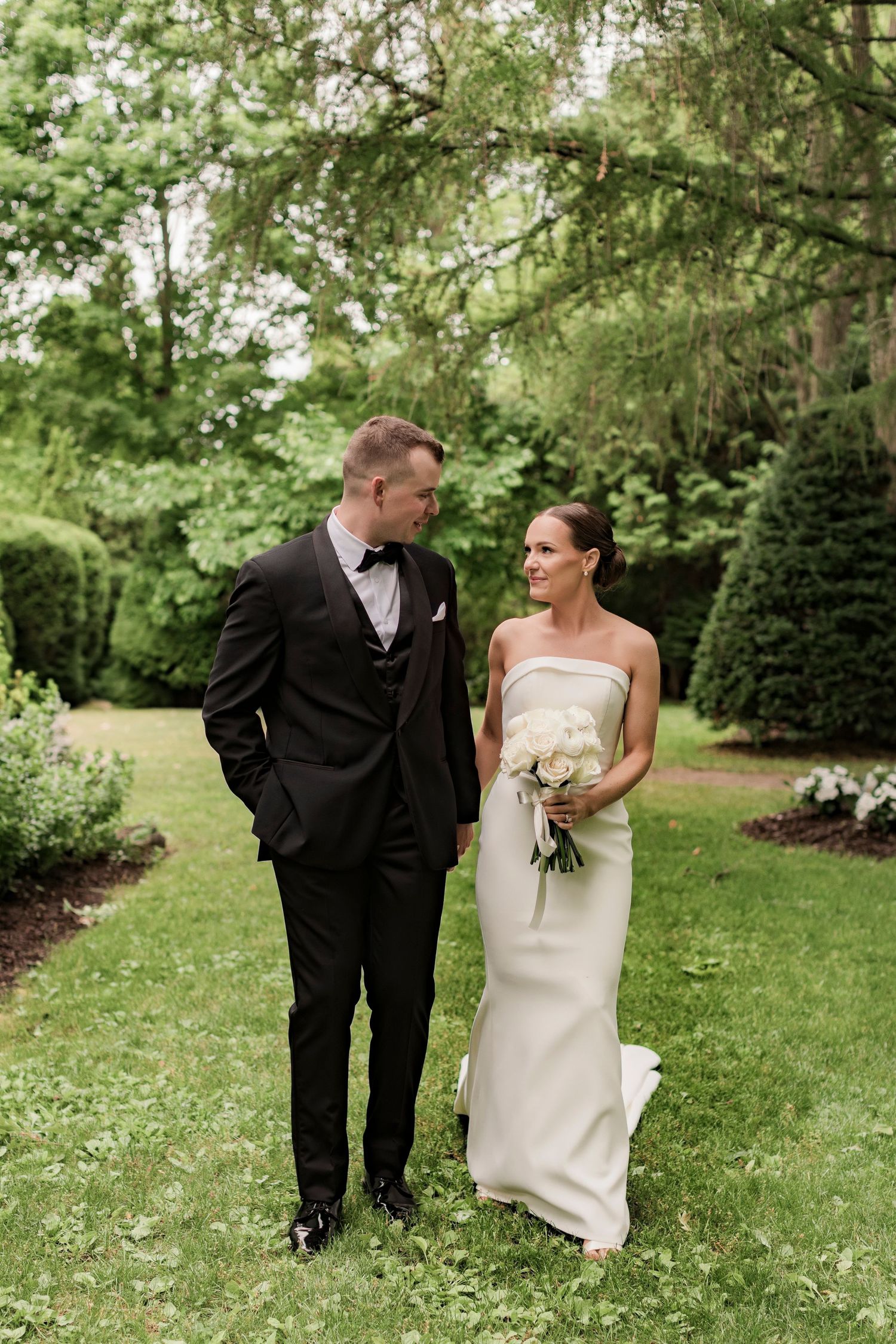 Intimate wedding portrait of couple in formal attire standing in green garden setting.