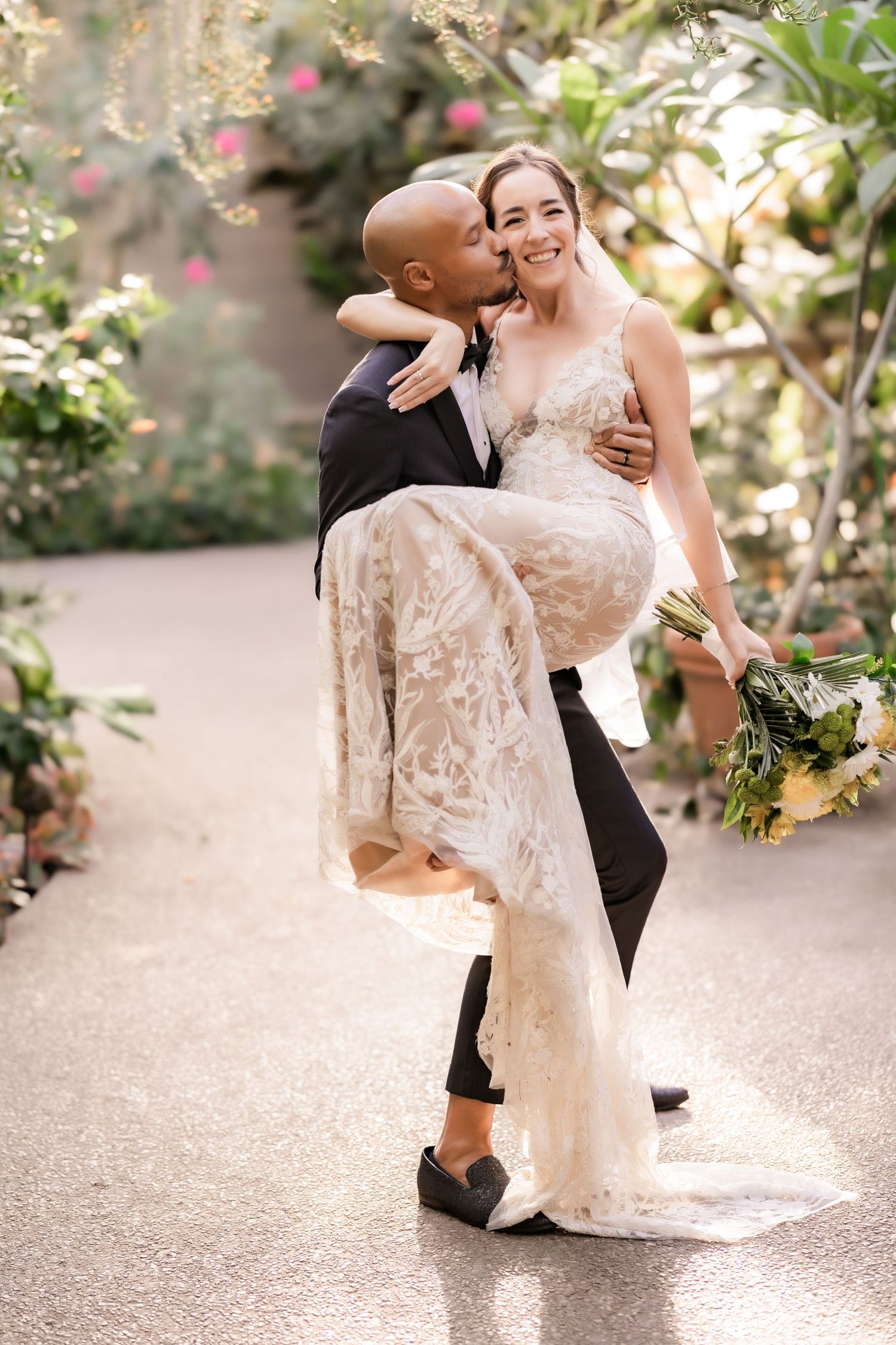 A playful wedding portrait with the groom lifting the bride in a lush garden setting.