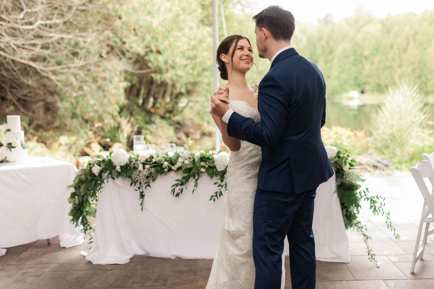A couple dancing together with decorative greenery garland in the background at their wedding.