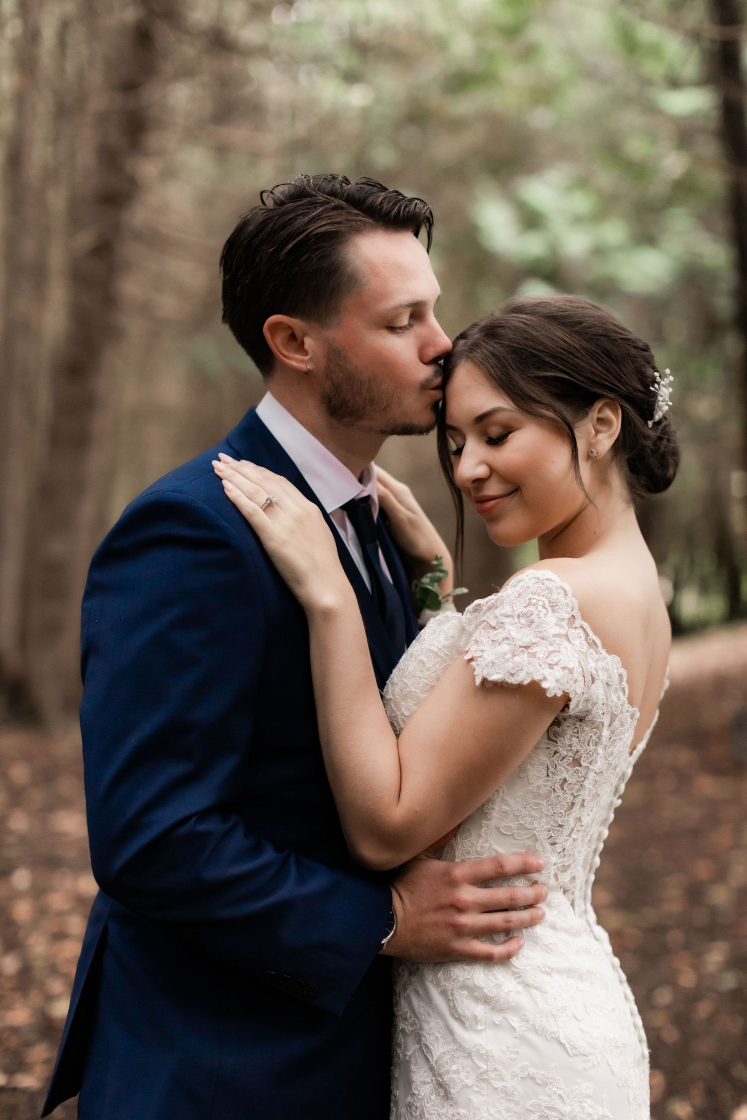 Romantic embrace between newlyweds in a wooded setting with soft natural lighting.