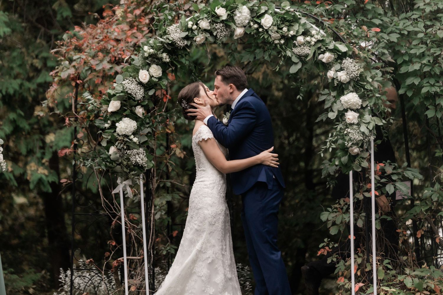 Romantic moment under floral arch with white roses during garden wedding ceremony.