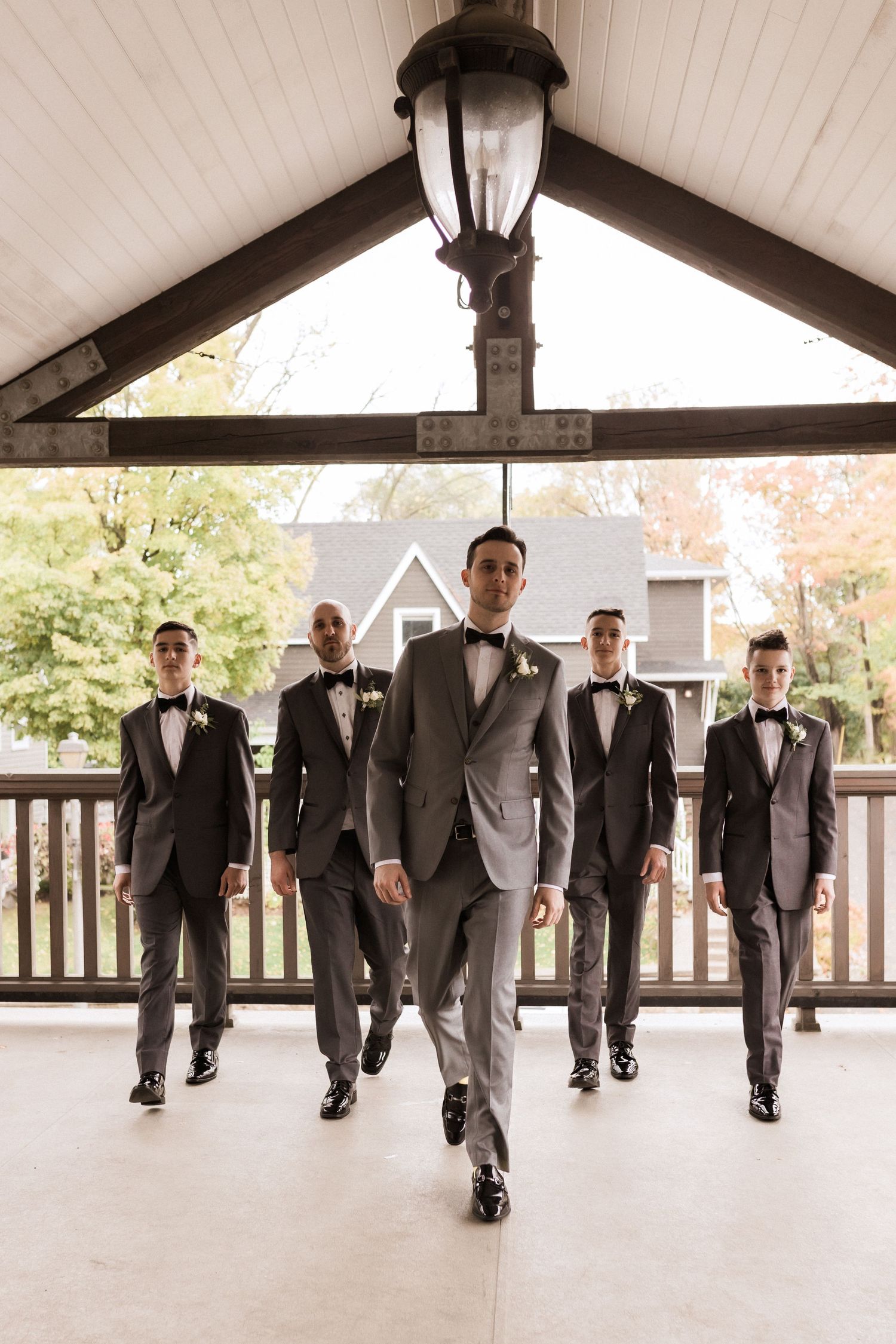 Groomsmen walk in formation with groom leading in light grey suit.