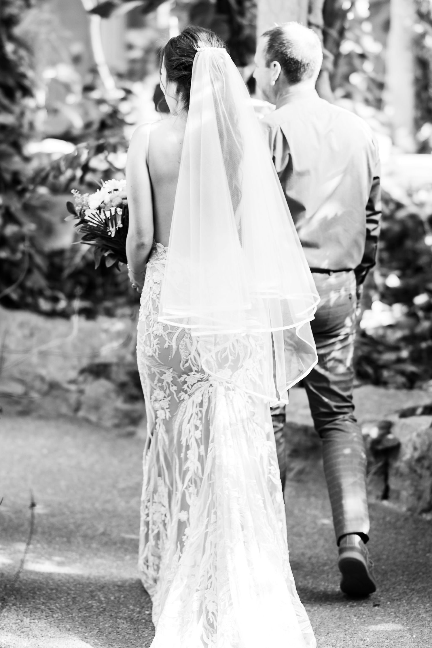 Back view of a couple walking down a garden path with the bride wearing a lace gown and veil.