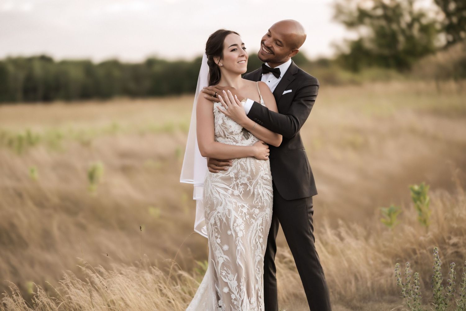 Joyful wedding couple shares a tender moment while standing in tall grass during their outdoor photo session.