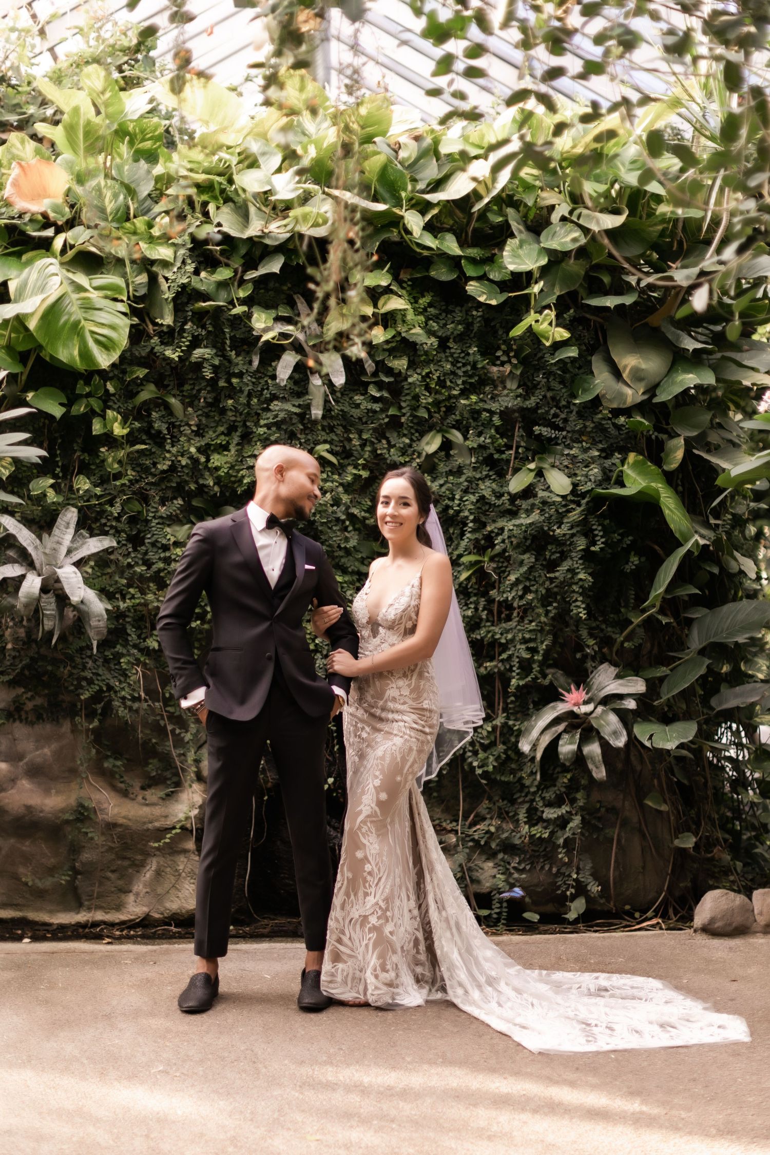 Wedding couple poses elegantly against a wall of tropical foliage for their portrait session.