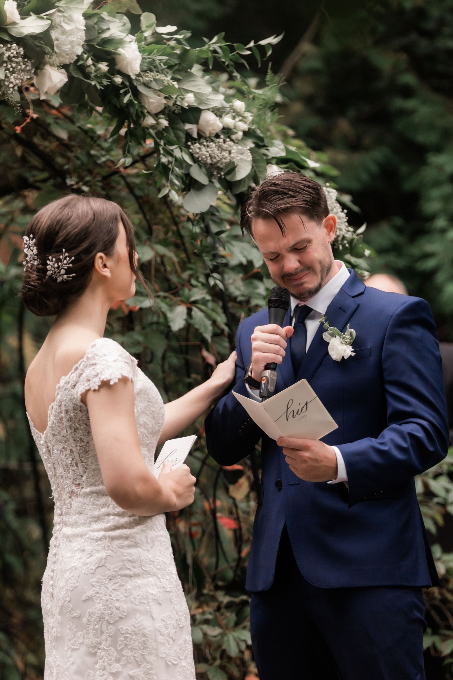 A bride and groom share an intimate moment while reading personal vows in a garden setting.